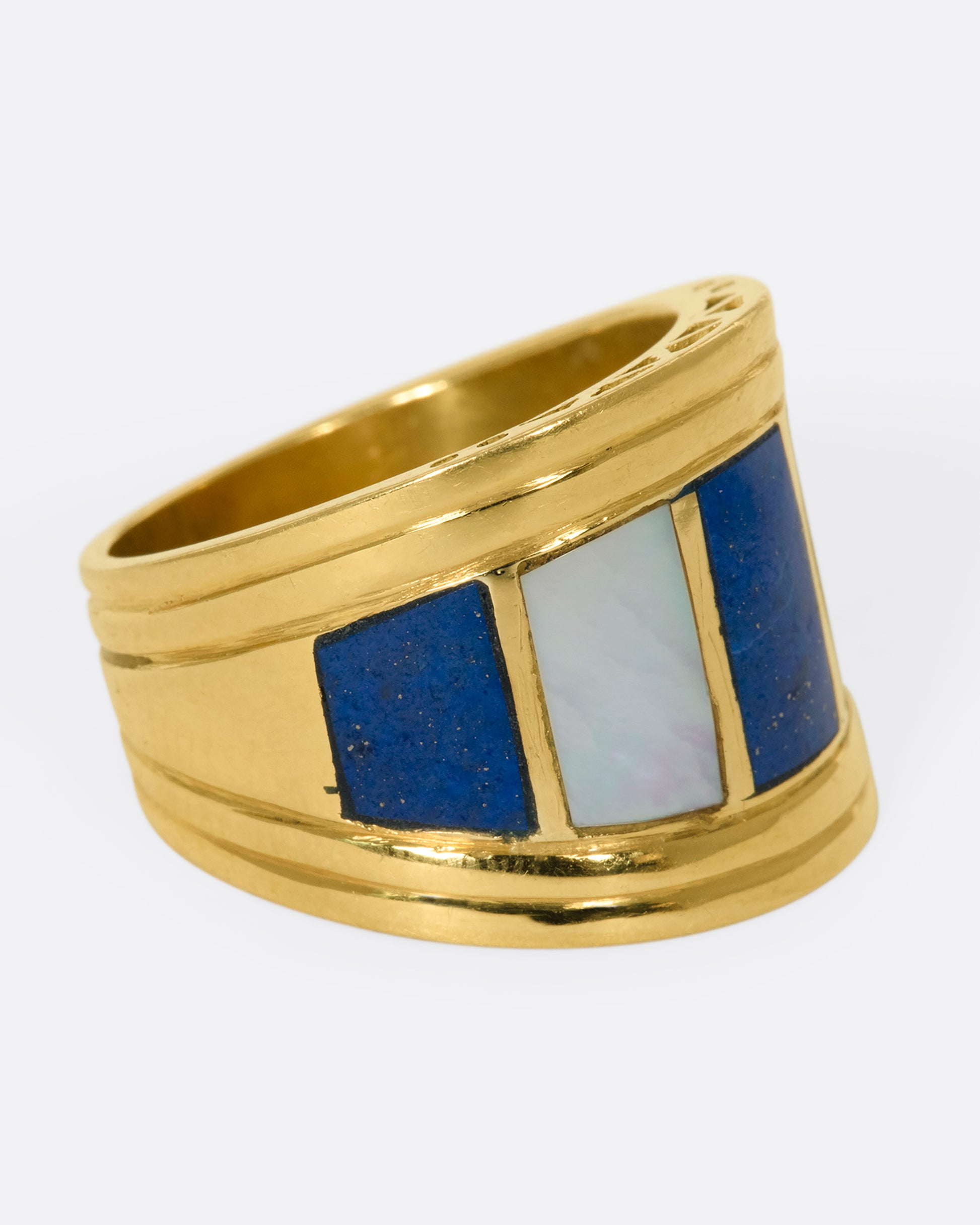 A right side view of a wide, tapered yellow gold ring with mother of pearl and lapis inlaid stripes.