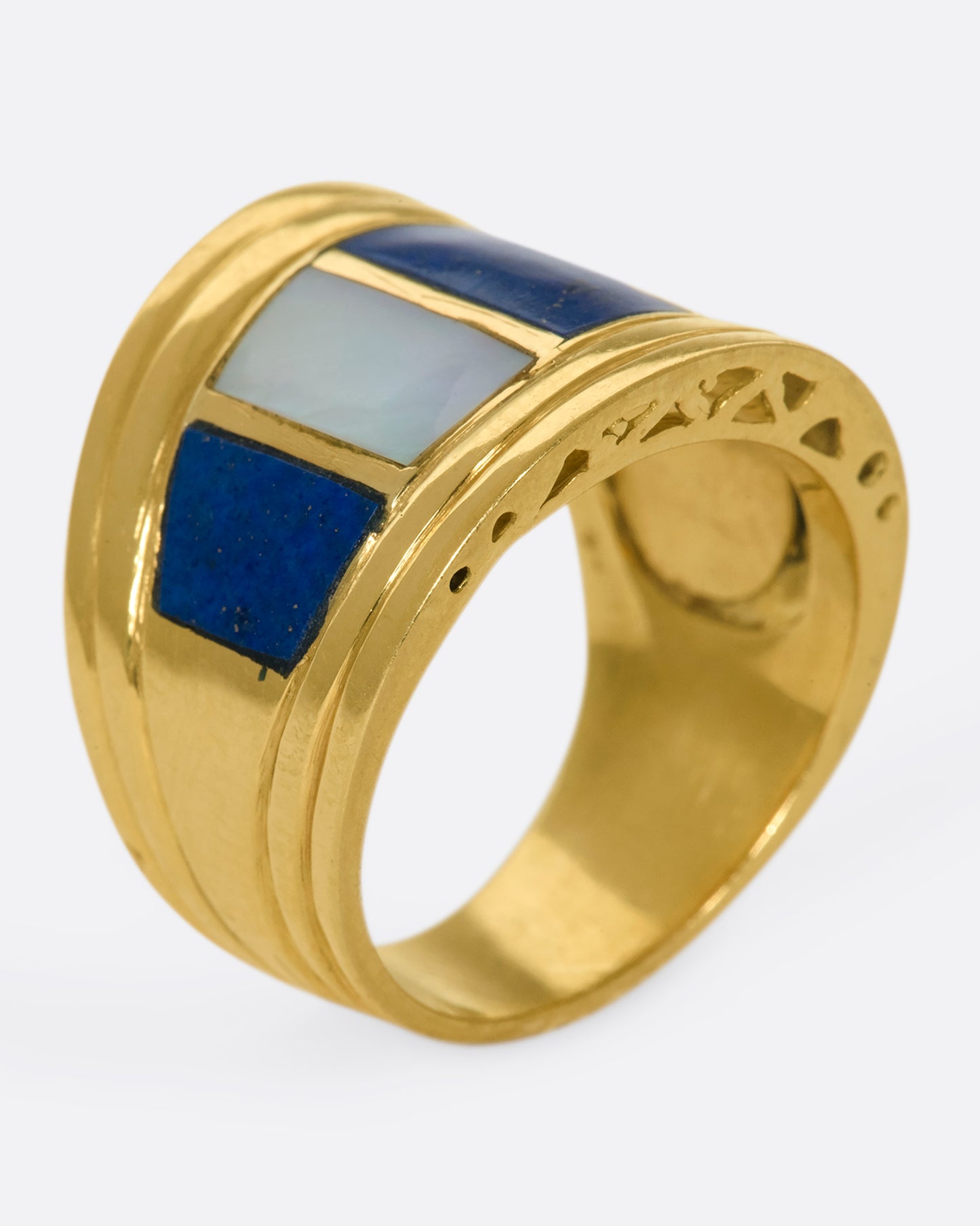 A view of a wide, tapered yellow gold ring with mother of pearl and lapis inlaid stripes standing up on its band.