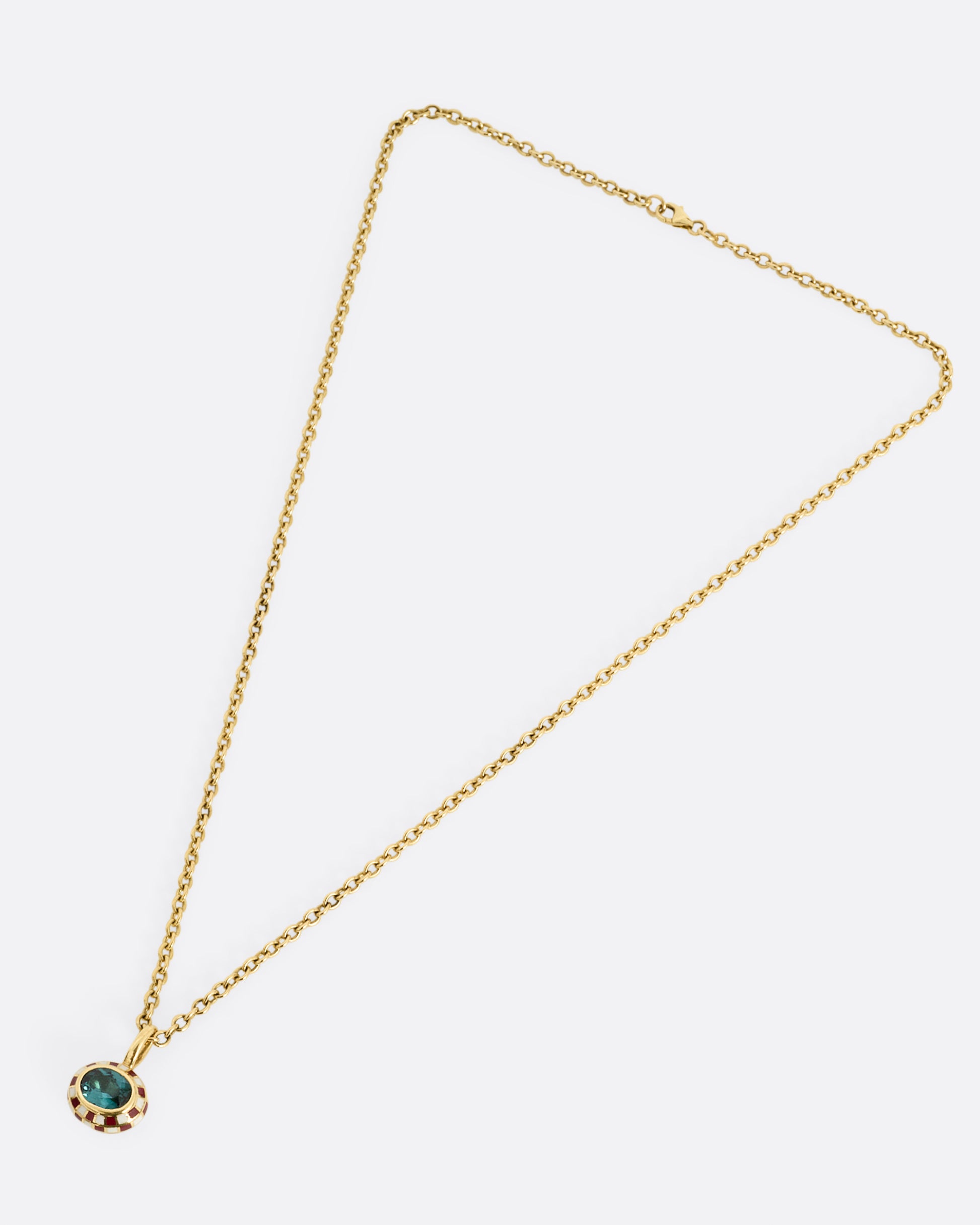 A yellow gold cable chain necklace with a red and cream enamel checkerboard pendant around a green tourmaline. The reverse side of the pendant has a checked pattern. Shown from the front.