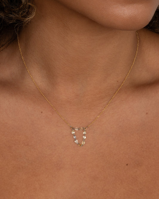 A close up of a yellow gold cable chain necklace with a loop of nine rose cut diamonds at the center. Shown worn.