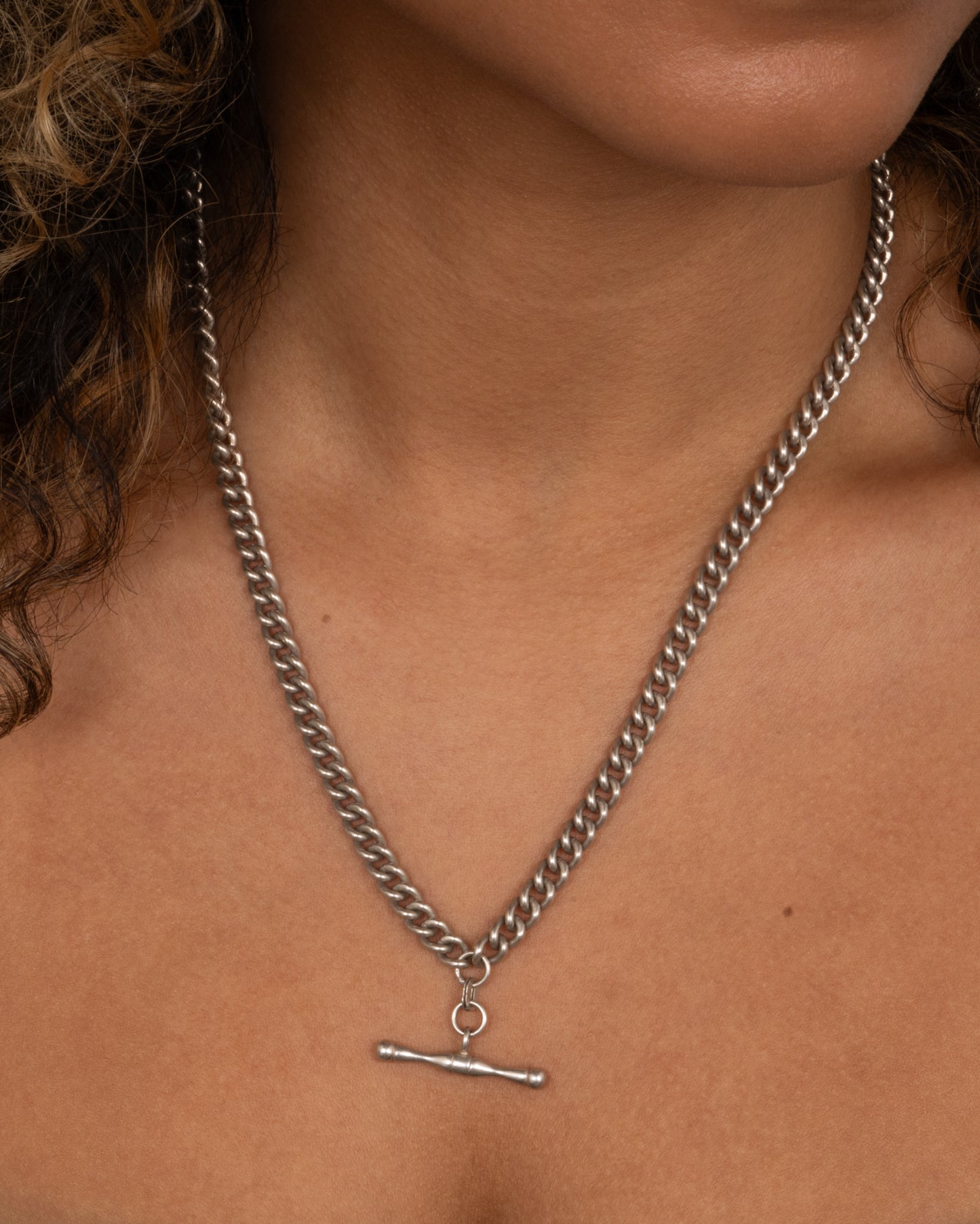 A silver curb chain pocket watch curb chain necklace with a T-bar on one end. Shown worn.