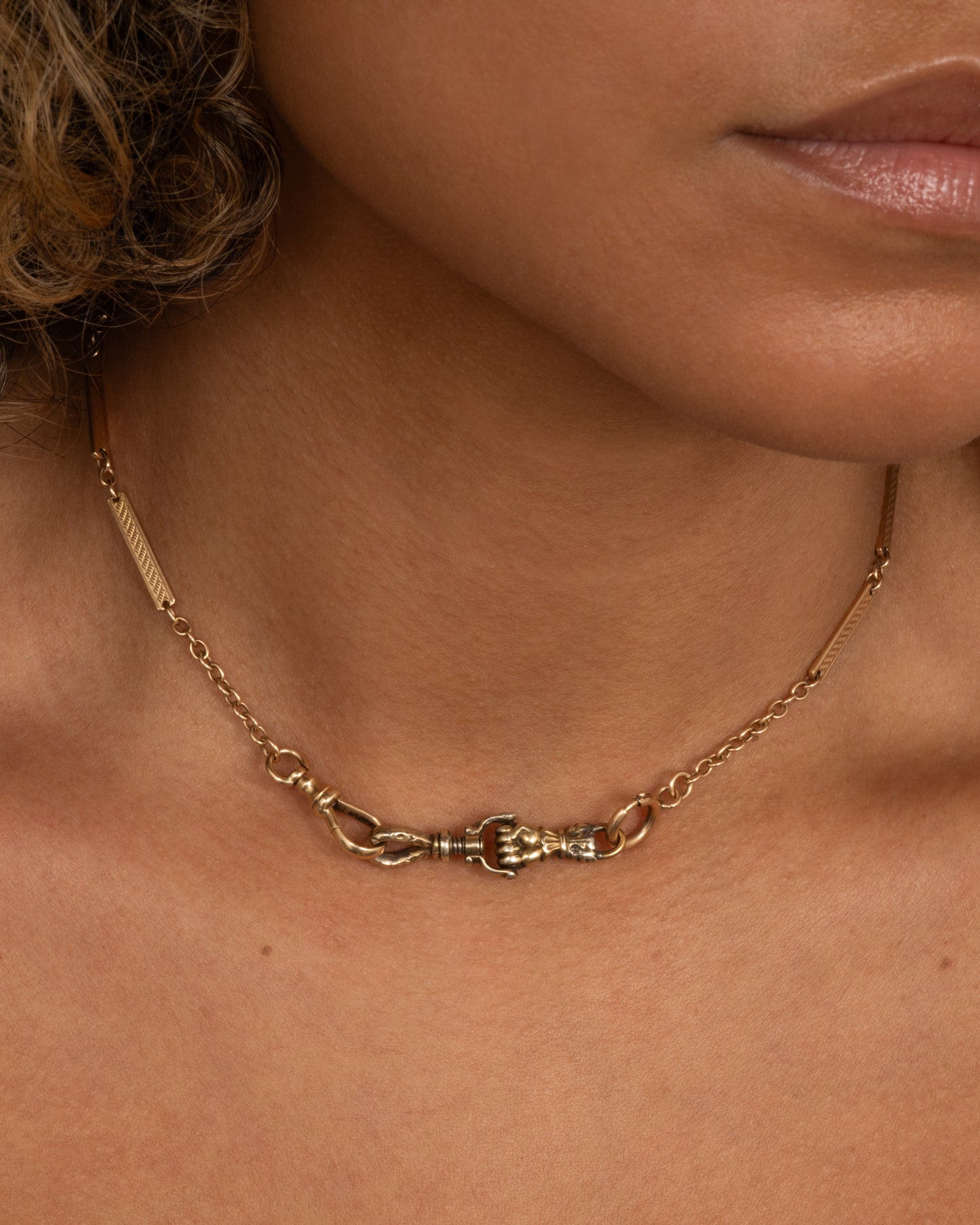 A yellow gold watch chain with textured elongated bar links. Shown with a victorian hand charm.