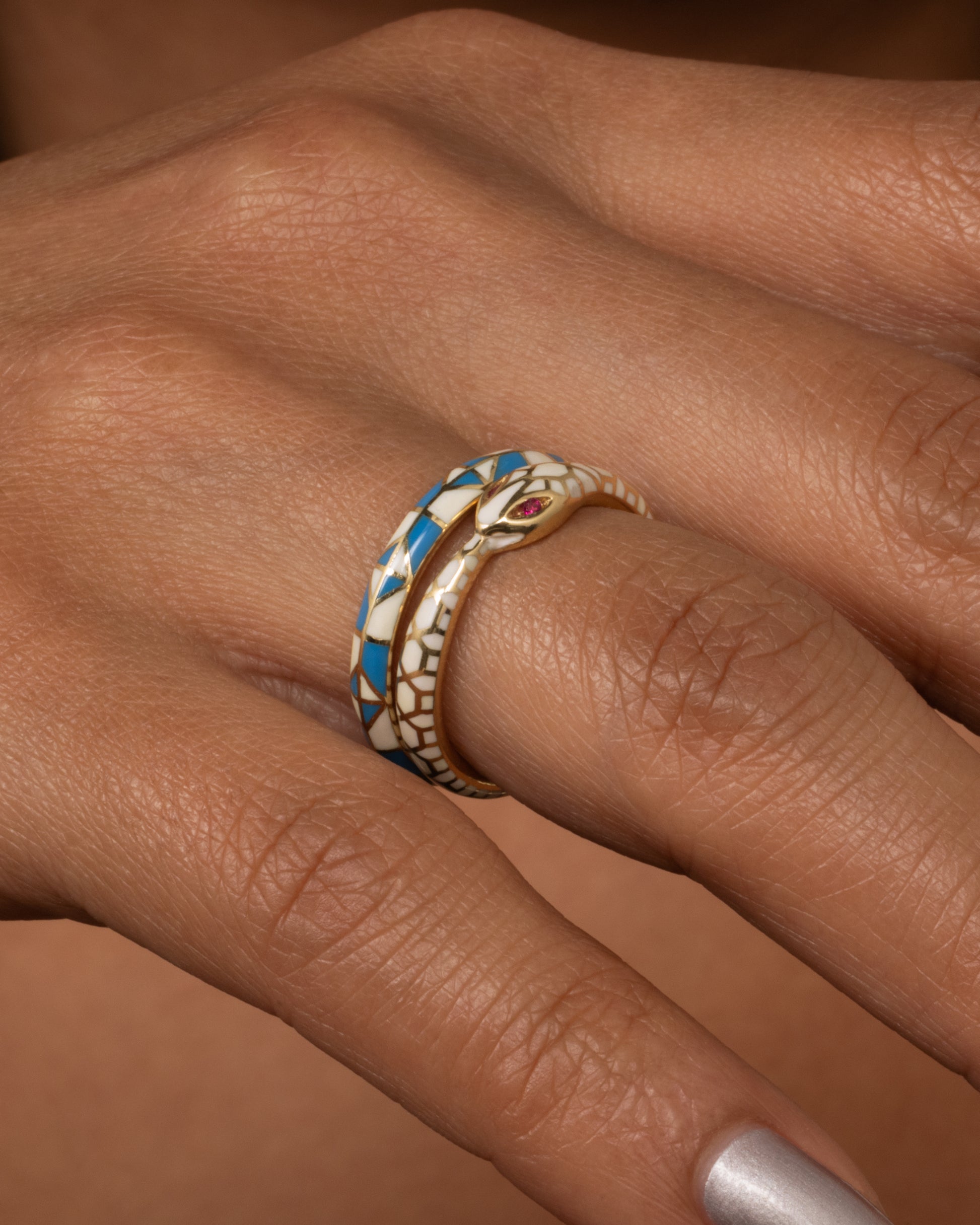 A yellow gold band ring with a turquoise and cream enamel patchwork pattern. Shown worn.