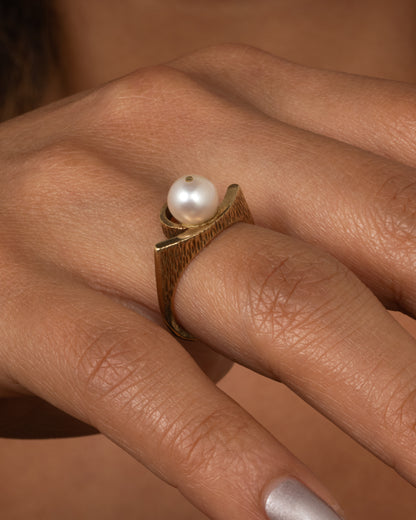 A yellow gold ring with a white pearl shown worn.