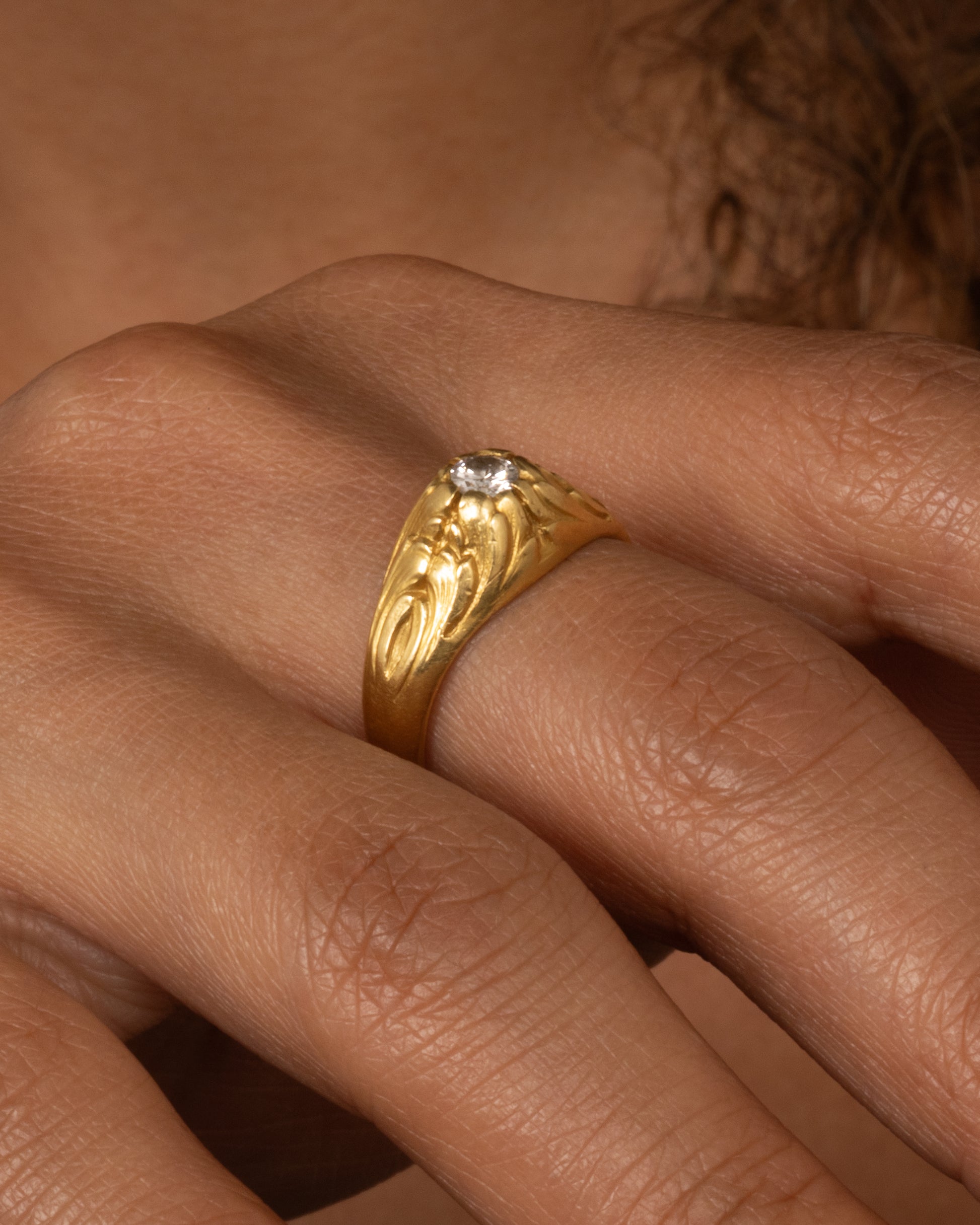 A yellow gold dome ring with  textural waves on its top and a round central diamond. Shown worn.