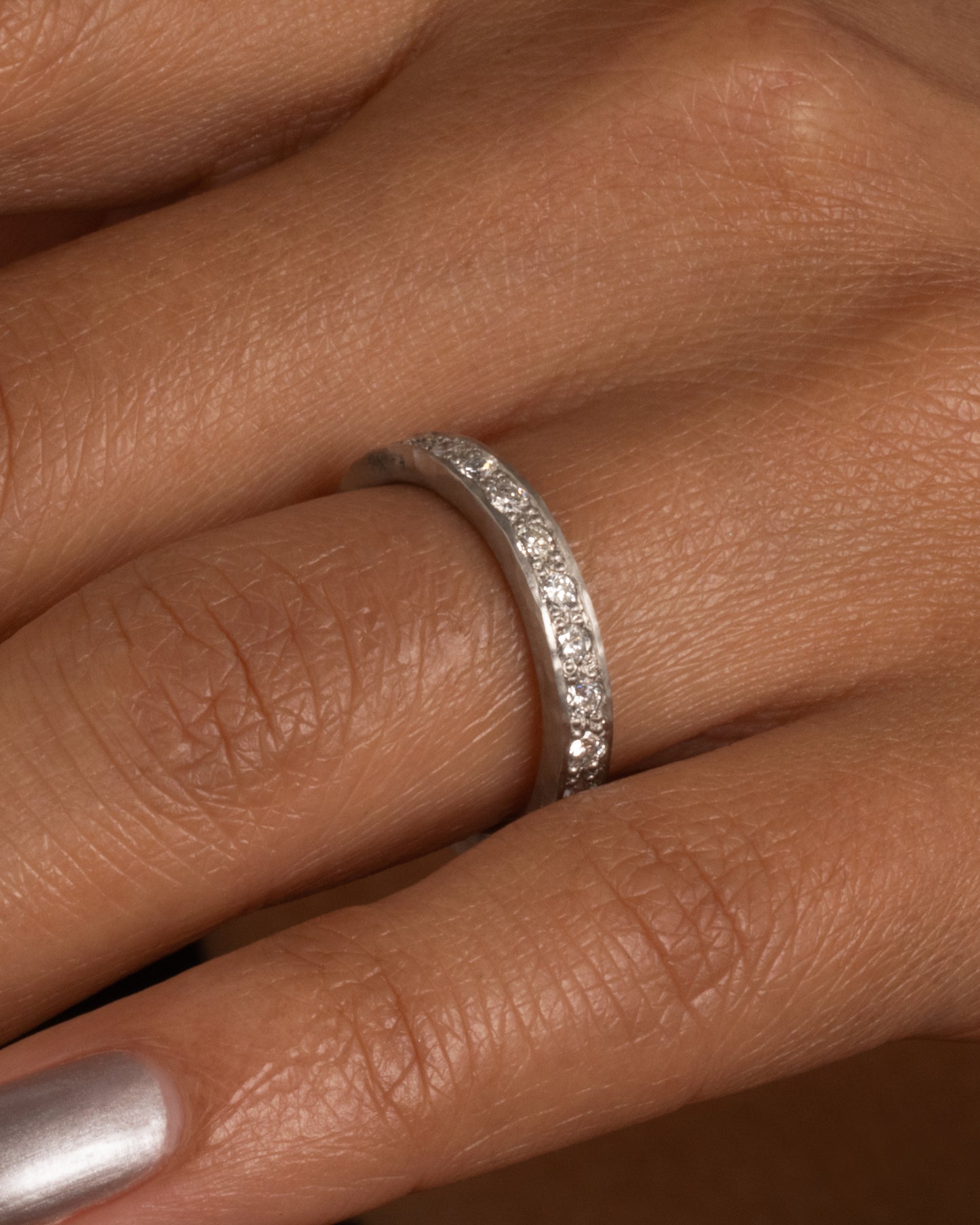 A platinum band with hammered edges and a darkened center with diamonds throughout. Shown worn
