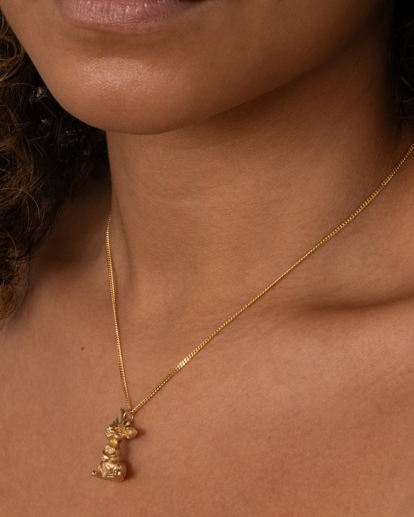 A yellow gold rabbit charm with one ear perked, sitting up. Shown worn.