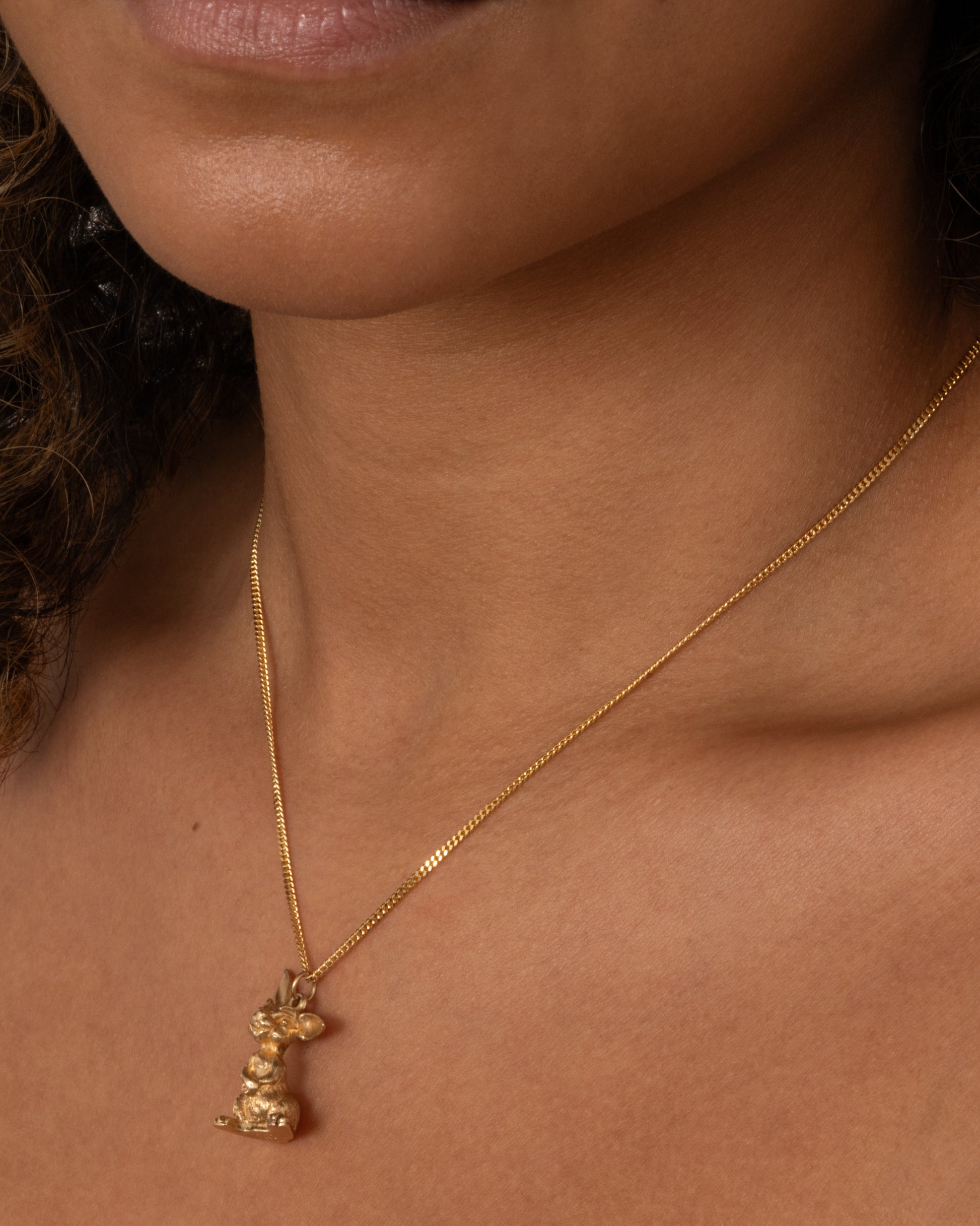 A yellow gold rabbit charm with one ear perked, sitting up. Shown worn.