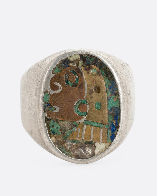 A silver ring with a brass and copper Aztec warrior mask set sodalite and turquoise. Shown from the front.