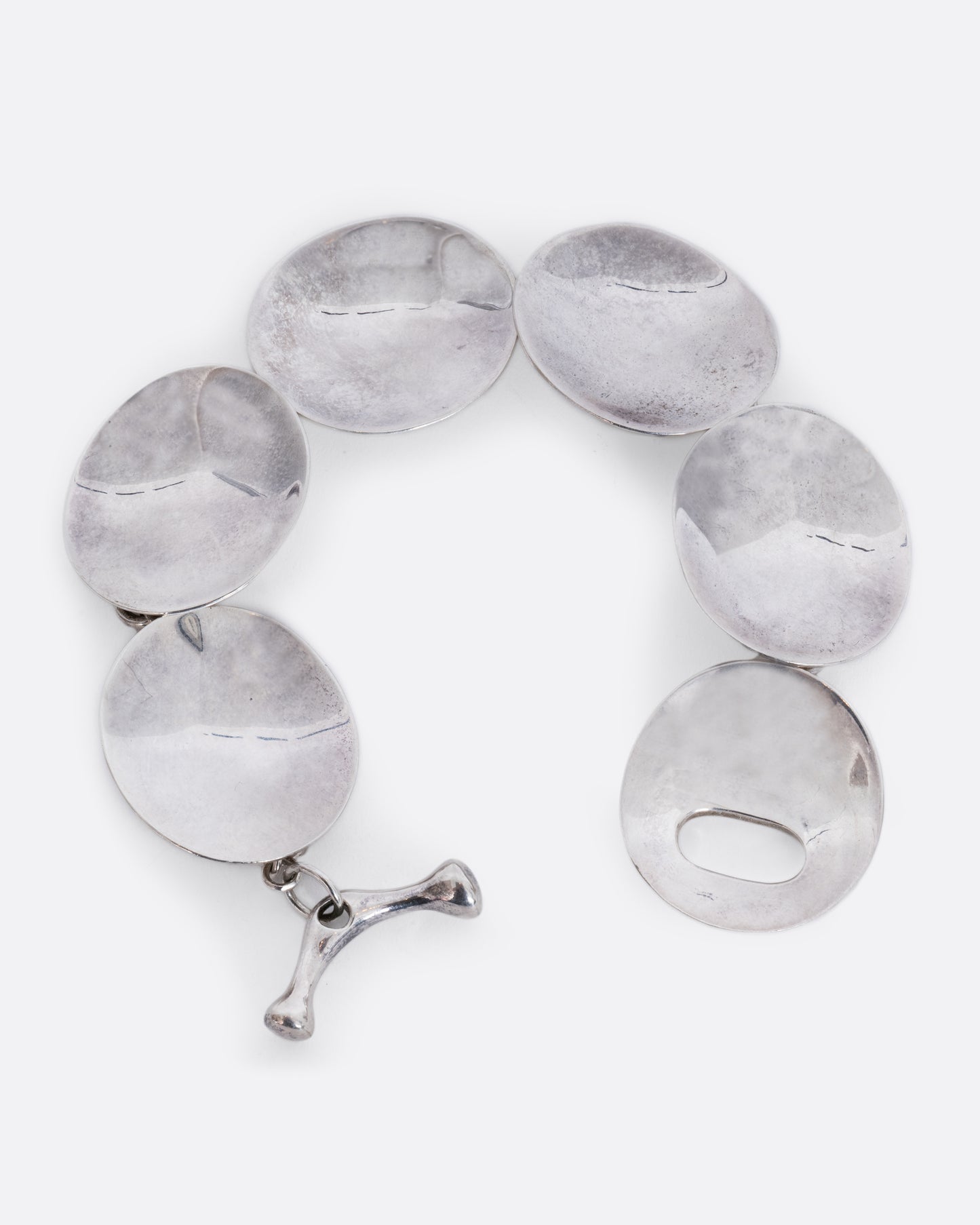 A sterling silver bracelet with concave circle links and a toggle closure. View laying flat with a close up of the closure.