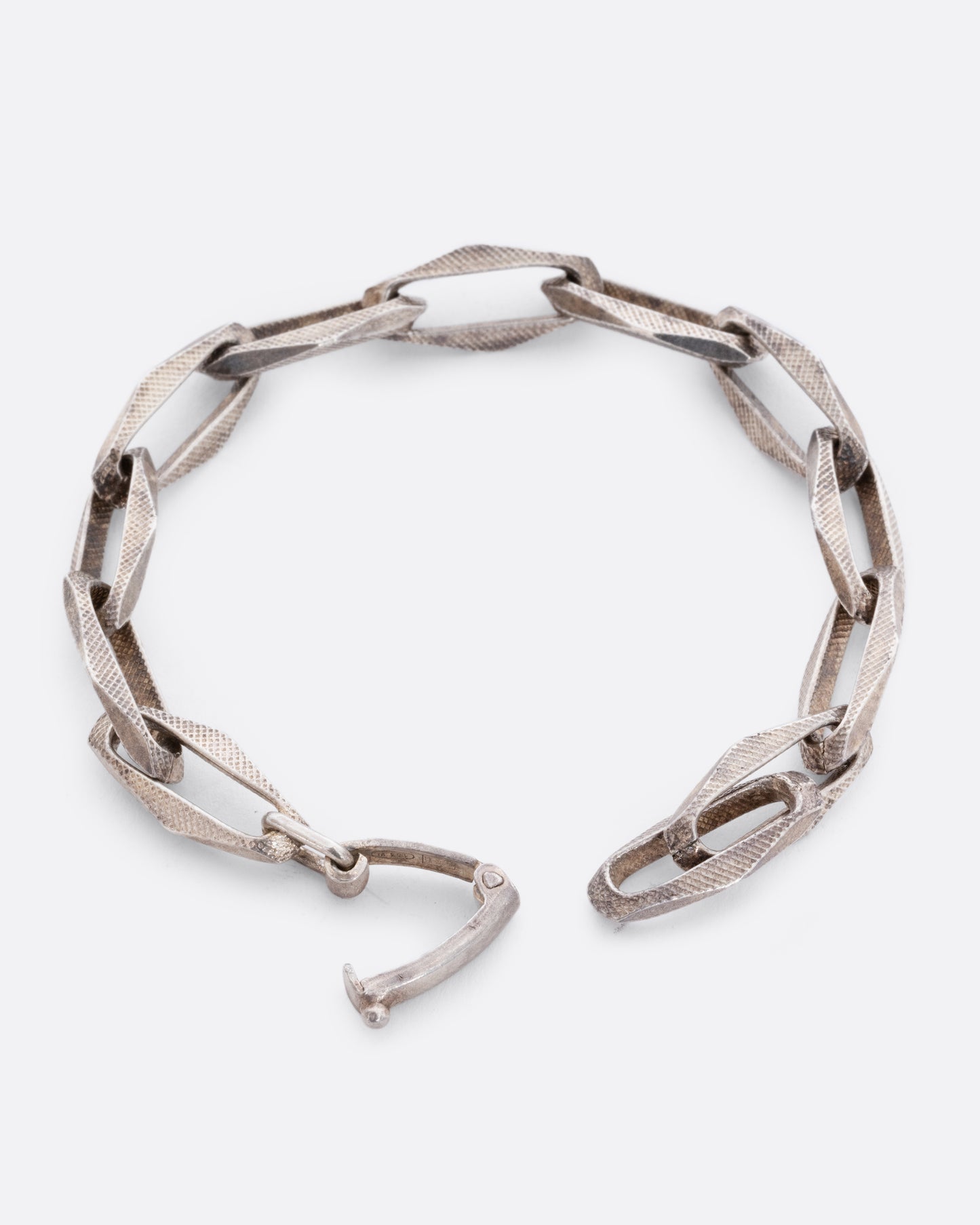 A sterling silver bracelet with textured geometric oval links. View open, showing the closure.