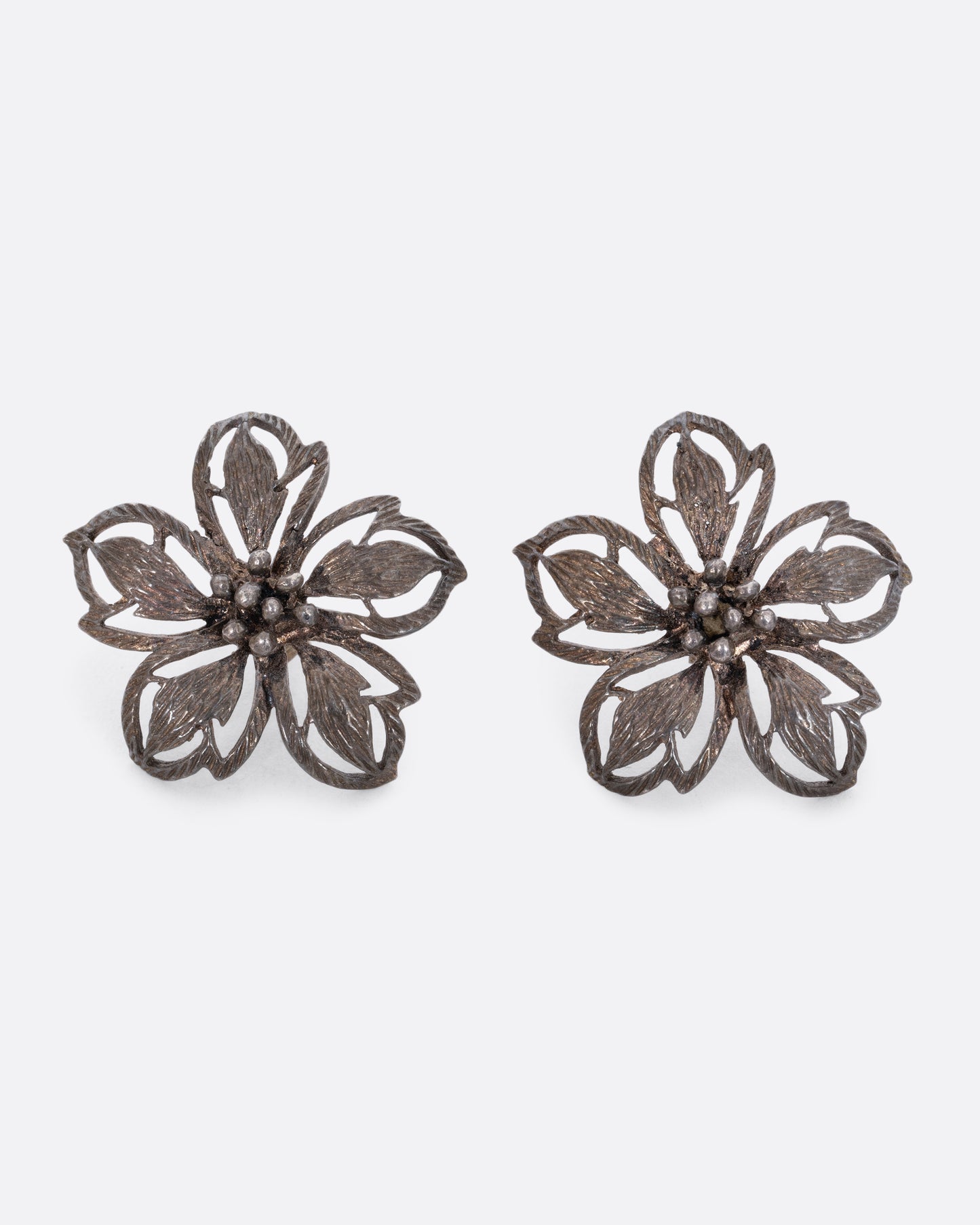 A pair of oxidized sterling openwork flower stud earrings. View from the front.