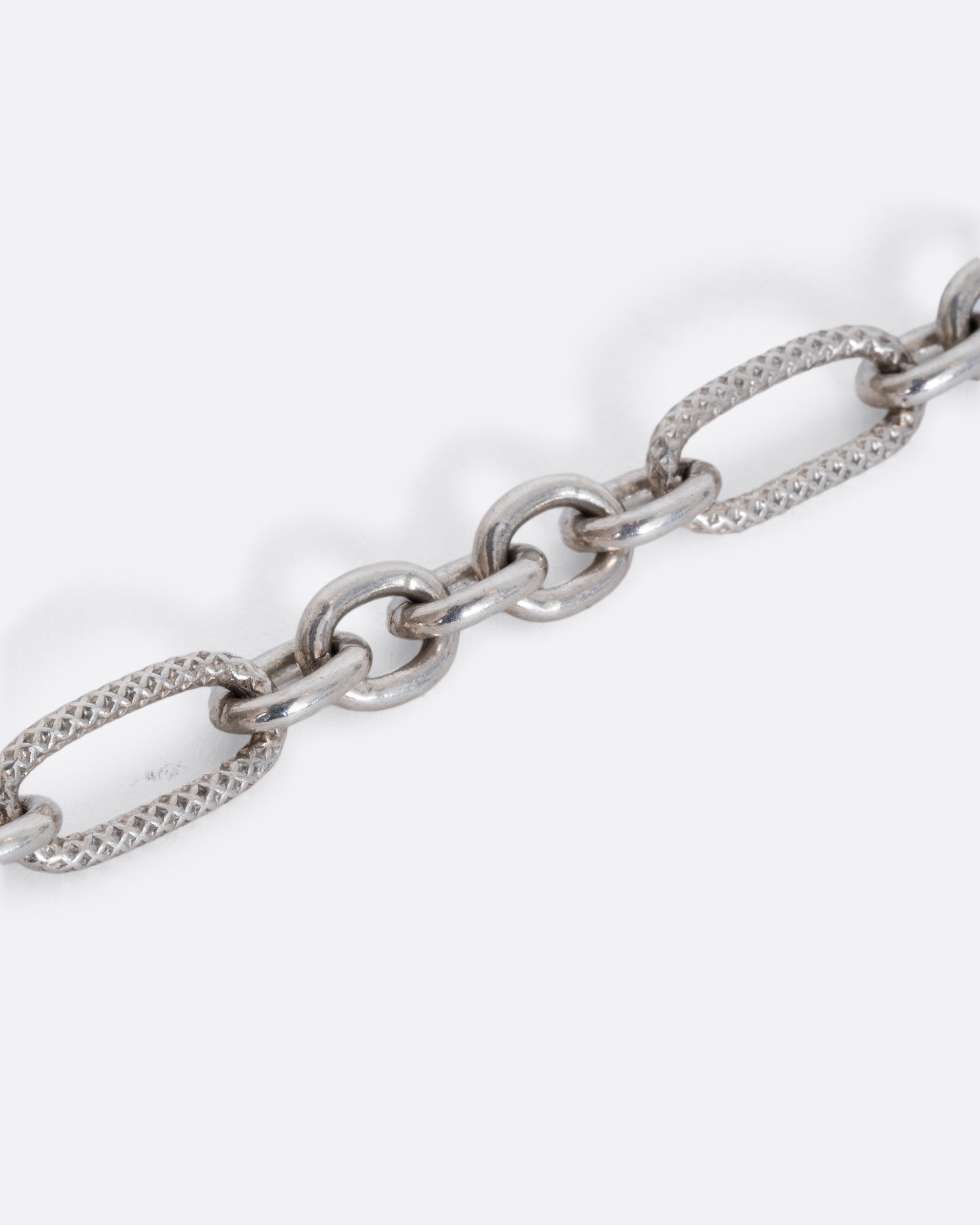 A lengthy textured oval cable chain necklace. View of the links close up.