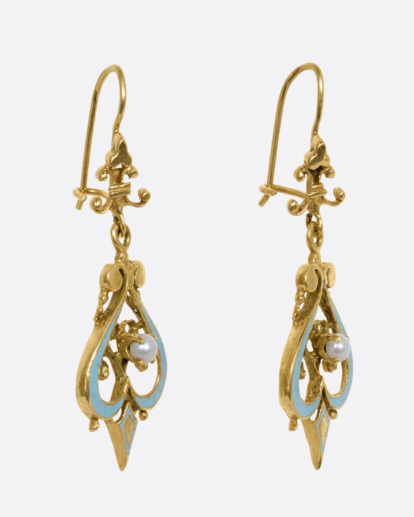 A pair of yellow gold filigree earrings with light blue enamel and pearls. Shown from the side.