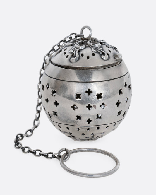 A sterling silver spherical tea infuser with botanical detail on lid. Shown from the front.