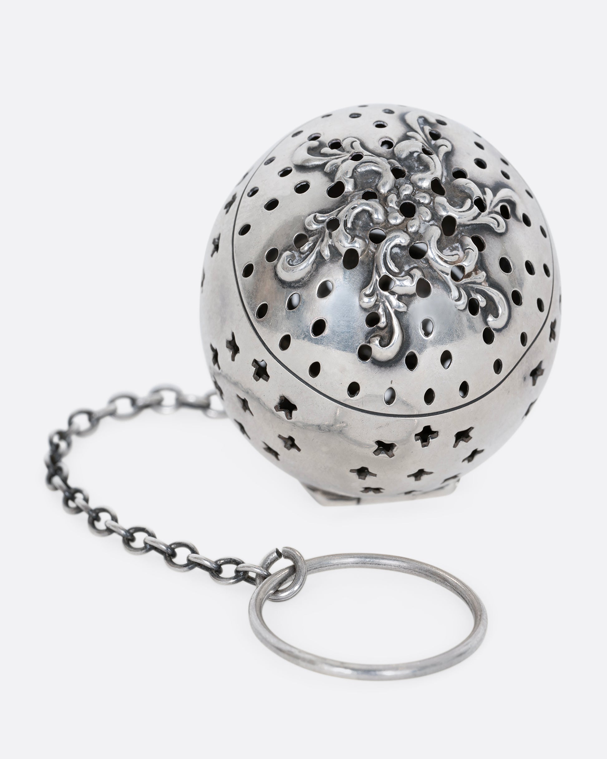 A sterling silver spherical tea infuser with botanical detail on lid. Shown from the top.