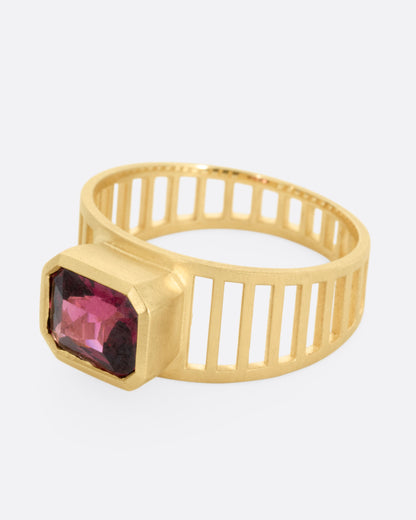 A yellow gold 'caged' band ring with a rhodolite garnet smolder, shown from the side.