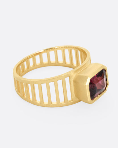 A yellow gold 'caged' band ring with a rhodolite garnet smolder, shown from the side.