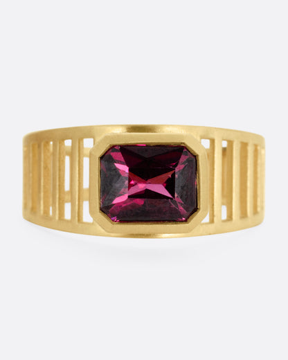 A yellow gold 'caged' band ring with a rhodolite garnet smolder, shown from the front.