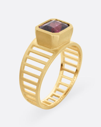 A yellow gold 'caged' band ring with a rhodolite garnet smolder, shown standing up from the side.