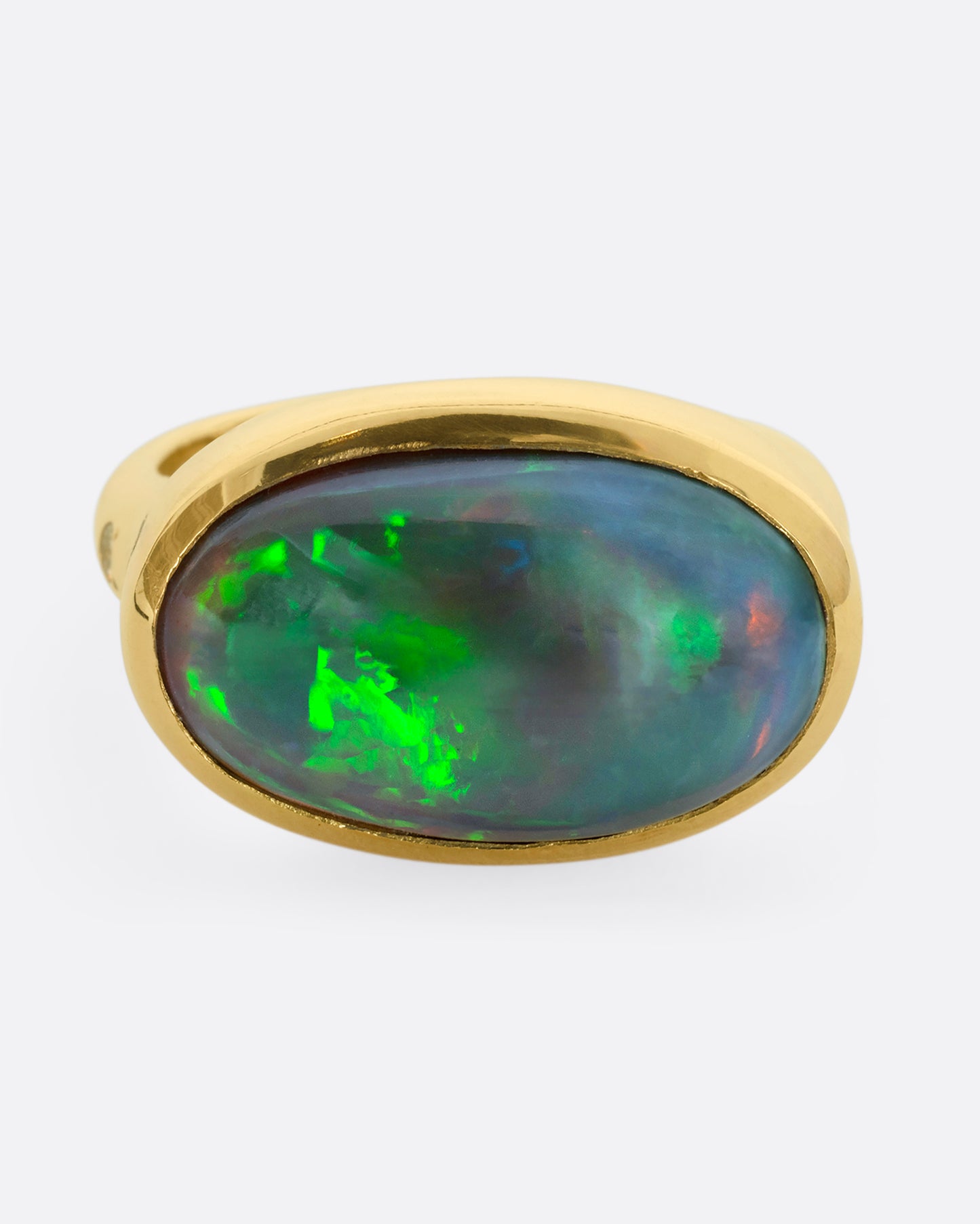 A yellow gold ring with a large oval opal at the center and diamonds on either shoulder. View from the front.