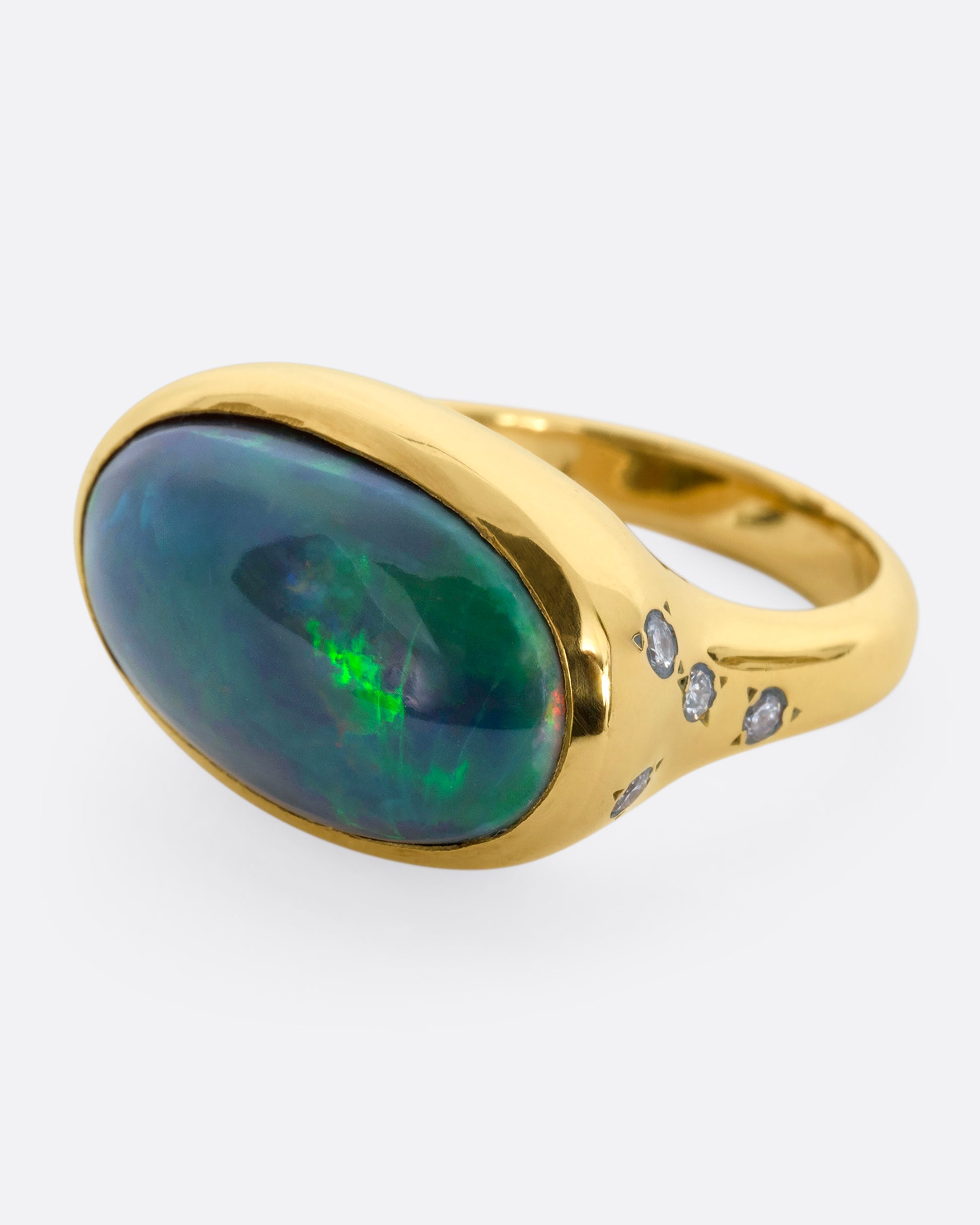 A yellow gold ring with a large oval opal at the center and diamonds on either shoulder. View from the side.