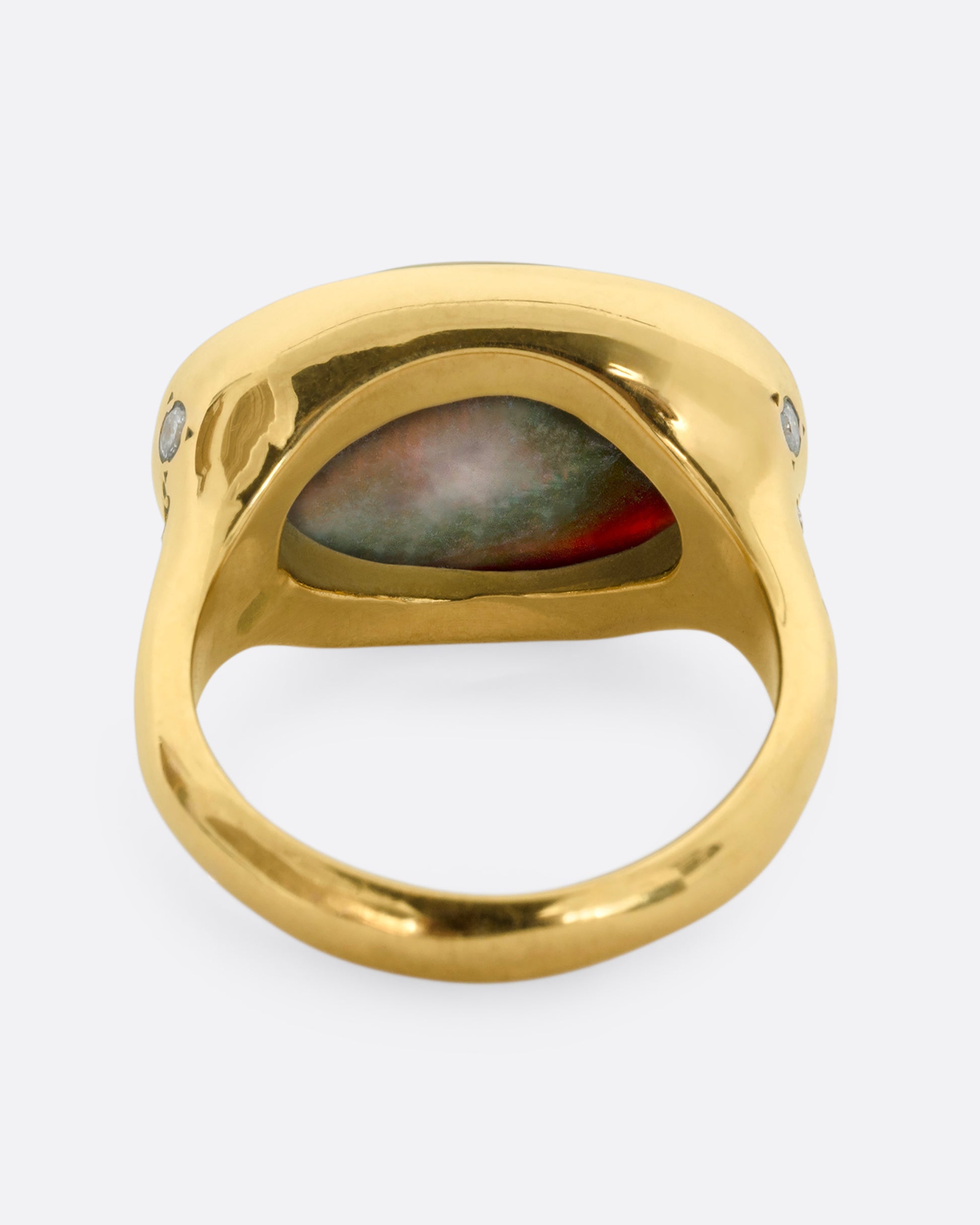 A yellow gold ring with a large oval opal at the center and diamonds on either shoulder. View from the back.