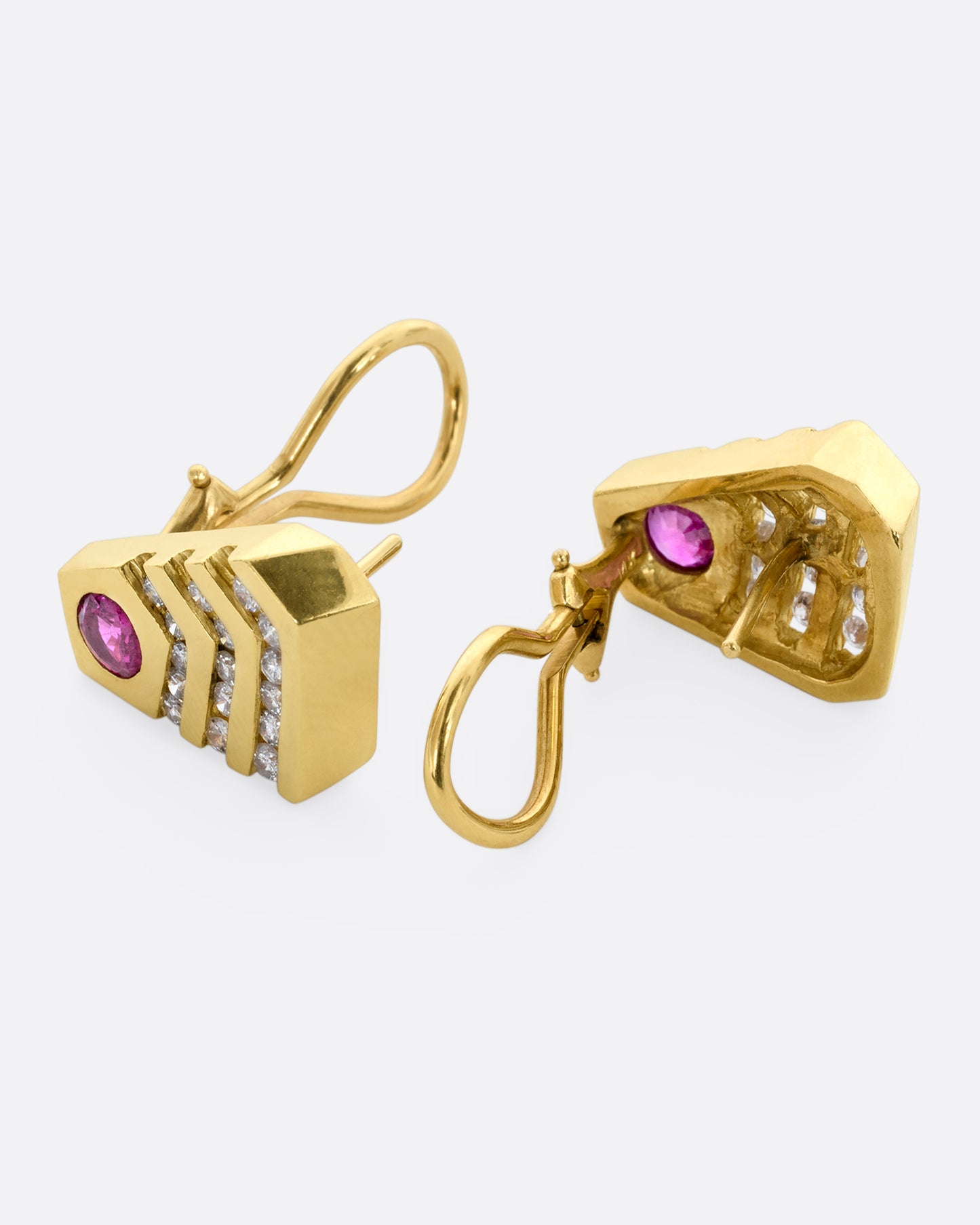 A pair of geometric yellow gold earrings with rubies and diamonds. View from the side, laying flat.