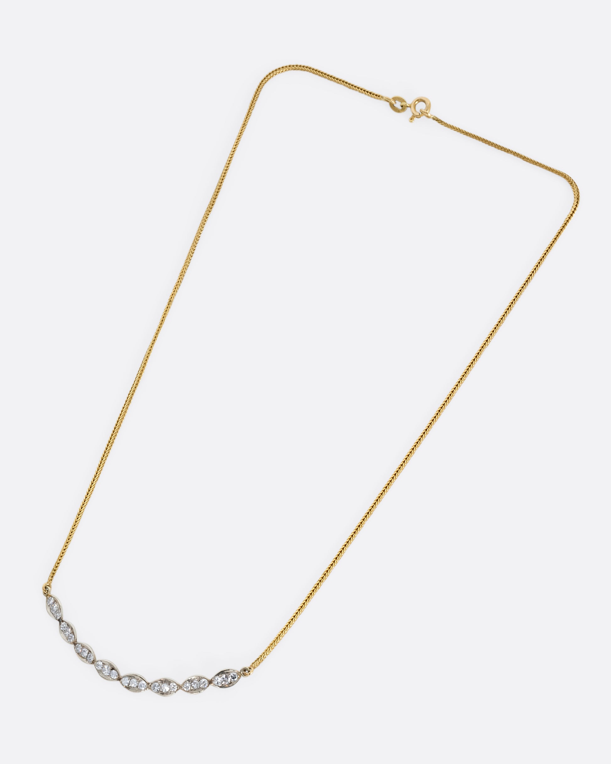 A white gold scallop edge curved bar necklace with diamonds on a yellow gold chain. View from above.