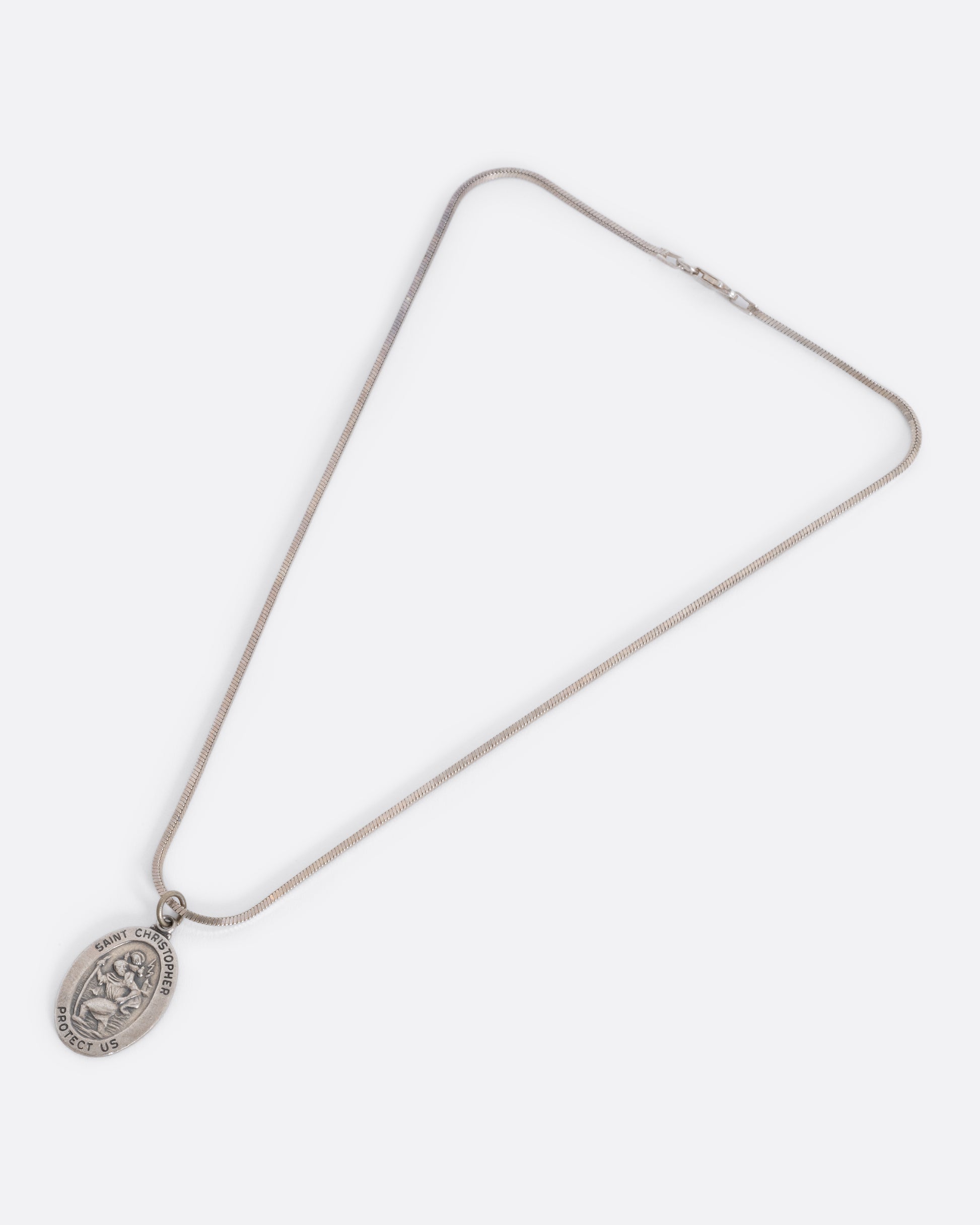 A sterling silver St. Christopher pendant hanging from a snake chain. View laying flat.