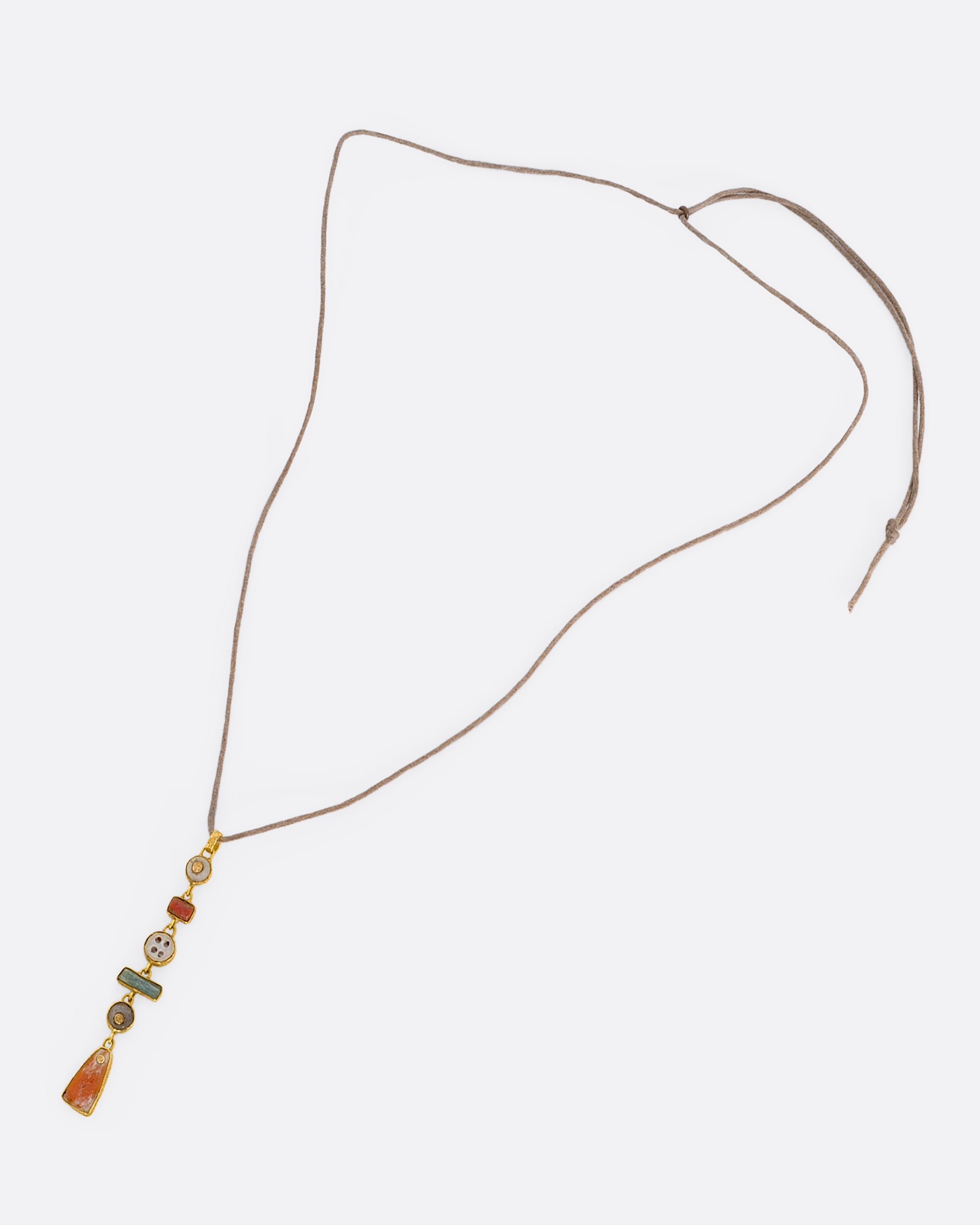 A tan cord necklace with six pre columbian elements hanging from it in a column, each wrapped in 22k gold. View laying flat.