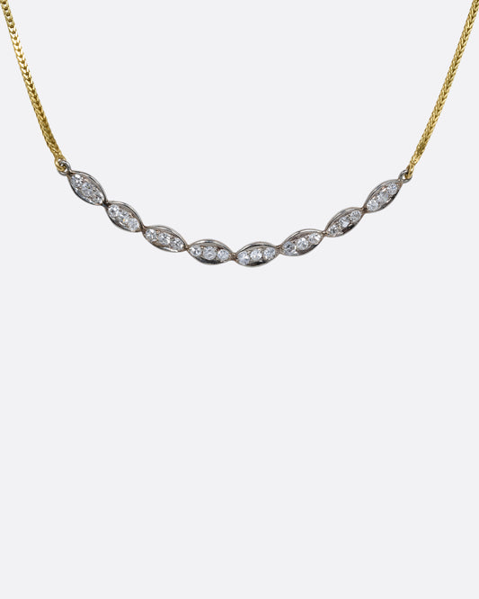 A white gold scallop edge curved bar necklace with diamonds on a yellow gold chain. View from the front.