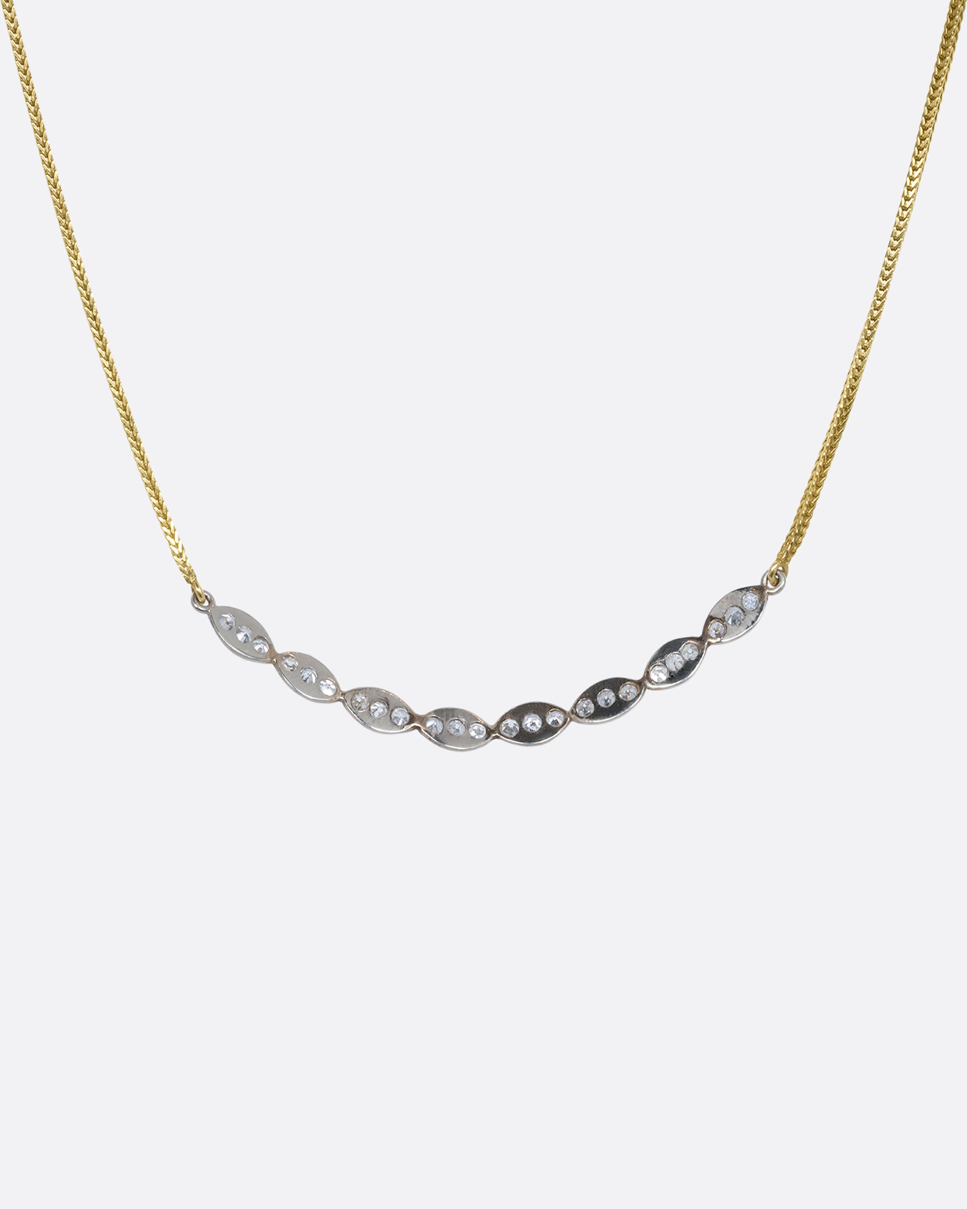 A white gold scallop edge curved bar necklace with diamonds on a yellow gold chain. View from the back.