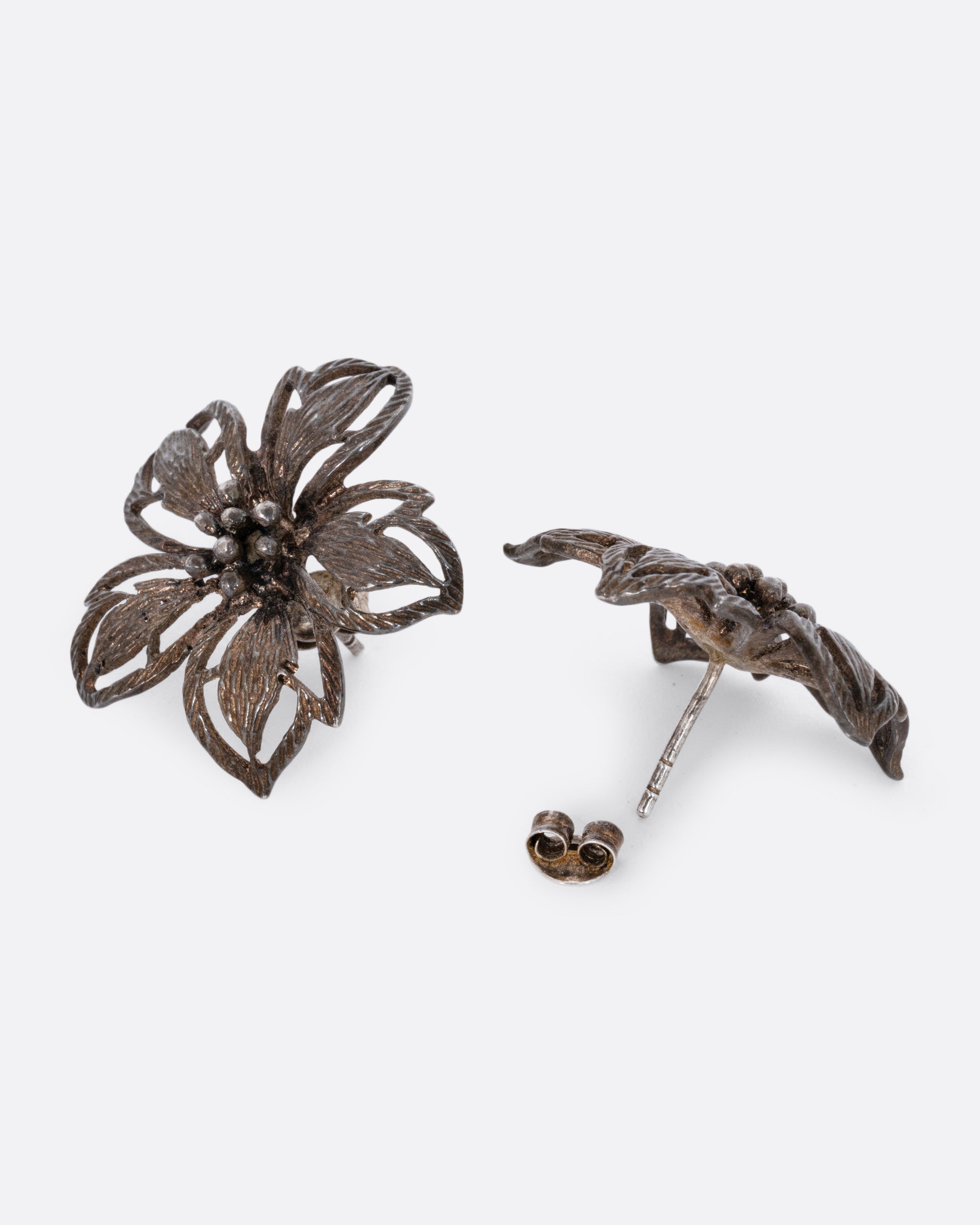 A pair of oxidized sterling openwork flower stud earrings. View alternating front and back.