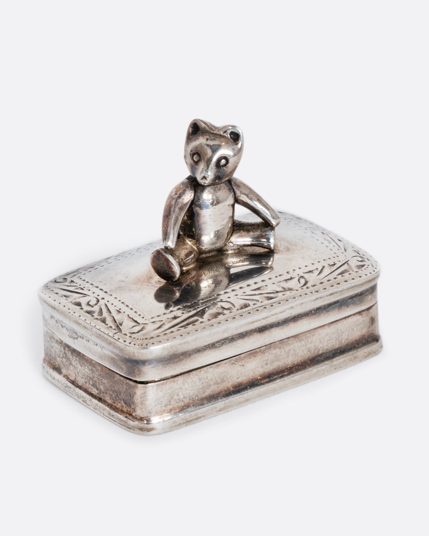 A sterling silver box with a swivel headed teddy bear on top. Shown from the side.