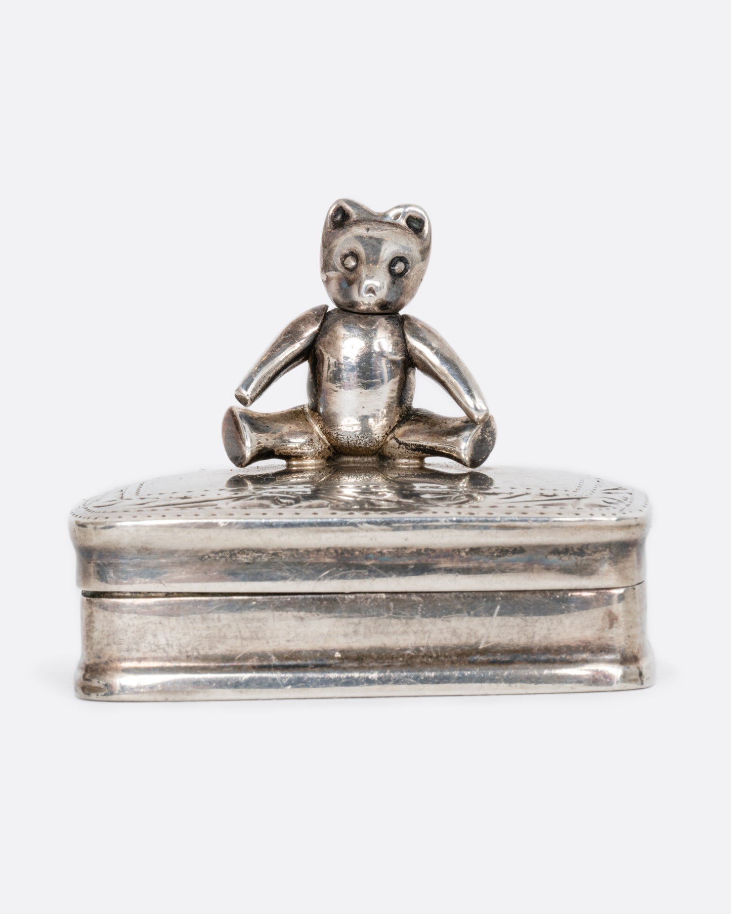 A sterling silver box with a swivel headed teddy bear on top. Shown from the front.