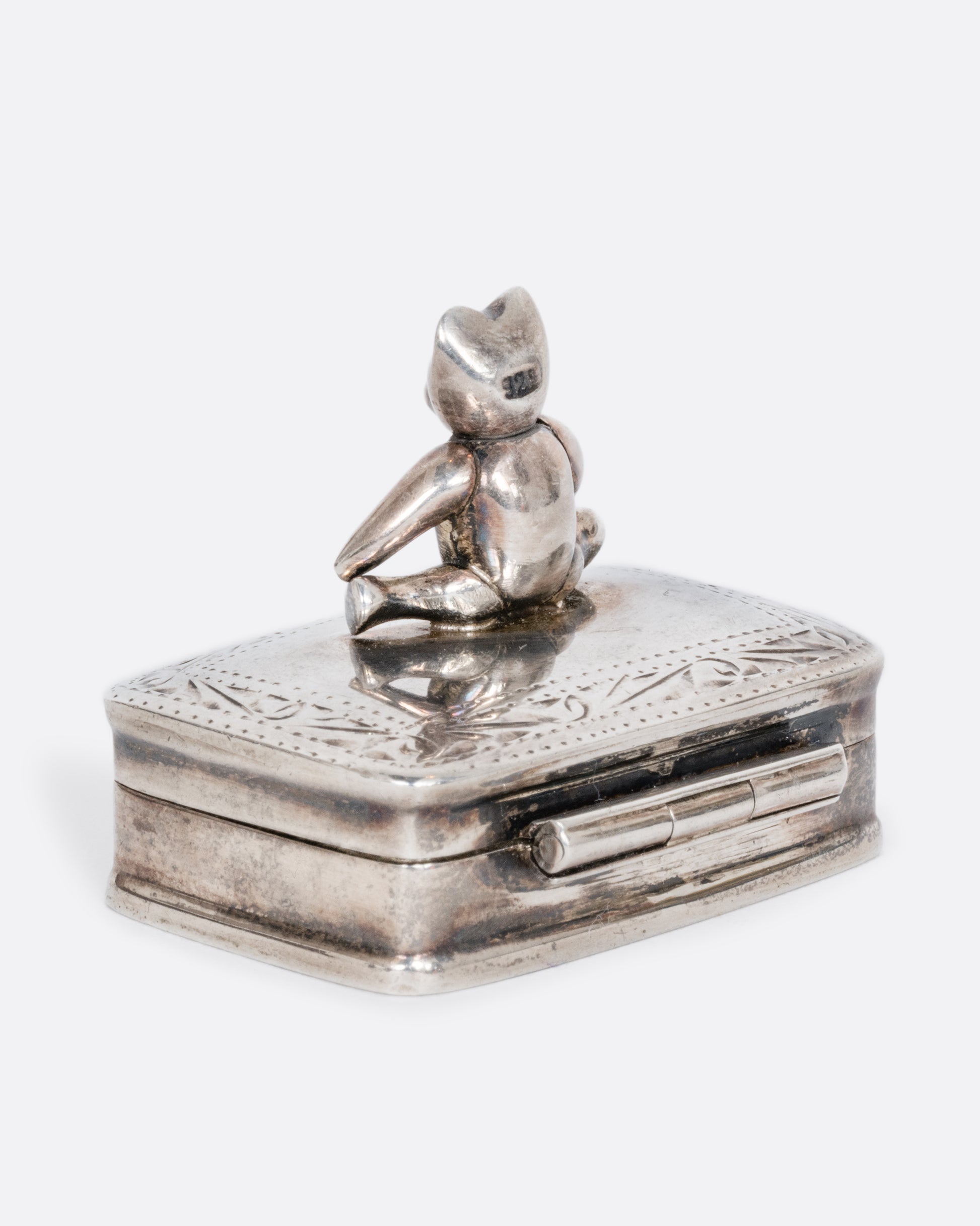 A sterling silver box with a swivel headed teddy bear on top. Shown from the back.