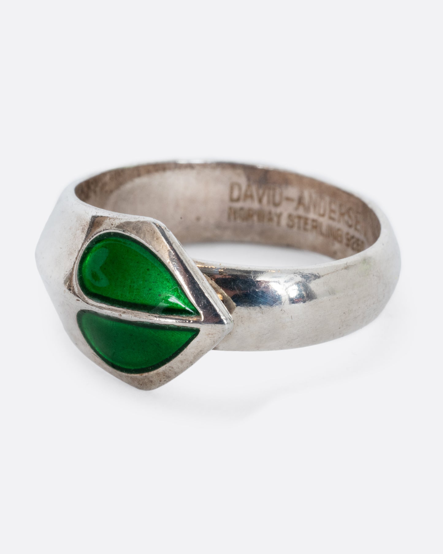 A sterling silver ring with a split green enamel heart. Shown from the side.