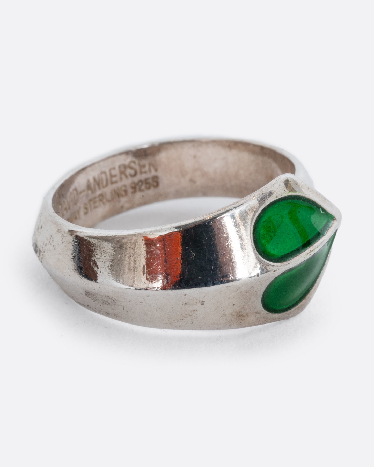 A sterling silver ring with a split green enamel heart. Shown from the side.