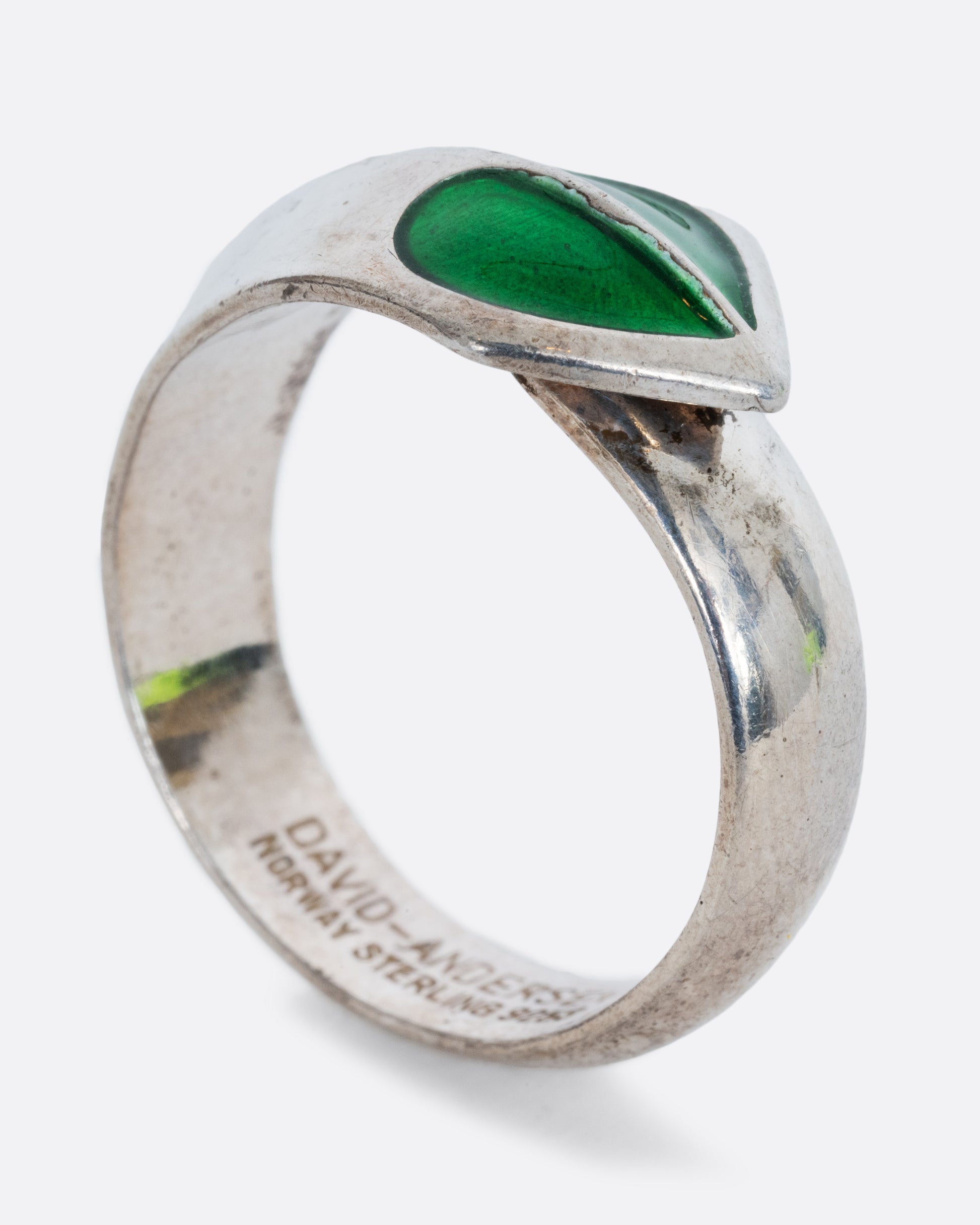 A sterling silver ring with a split green enamel heart. Shown from the side, standing up.