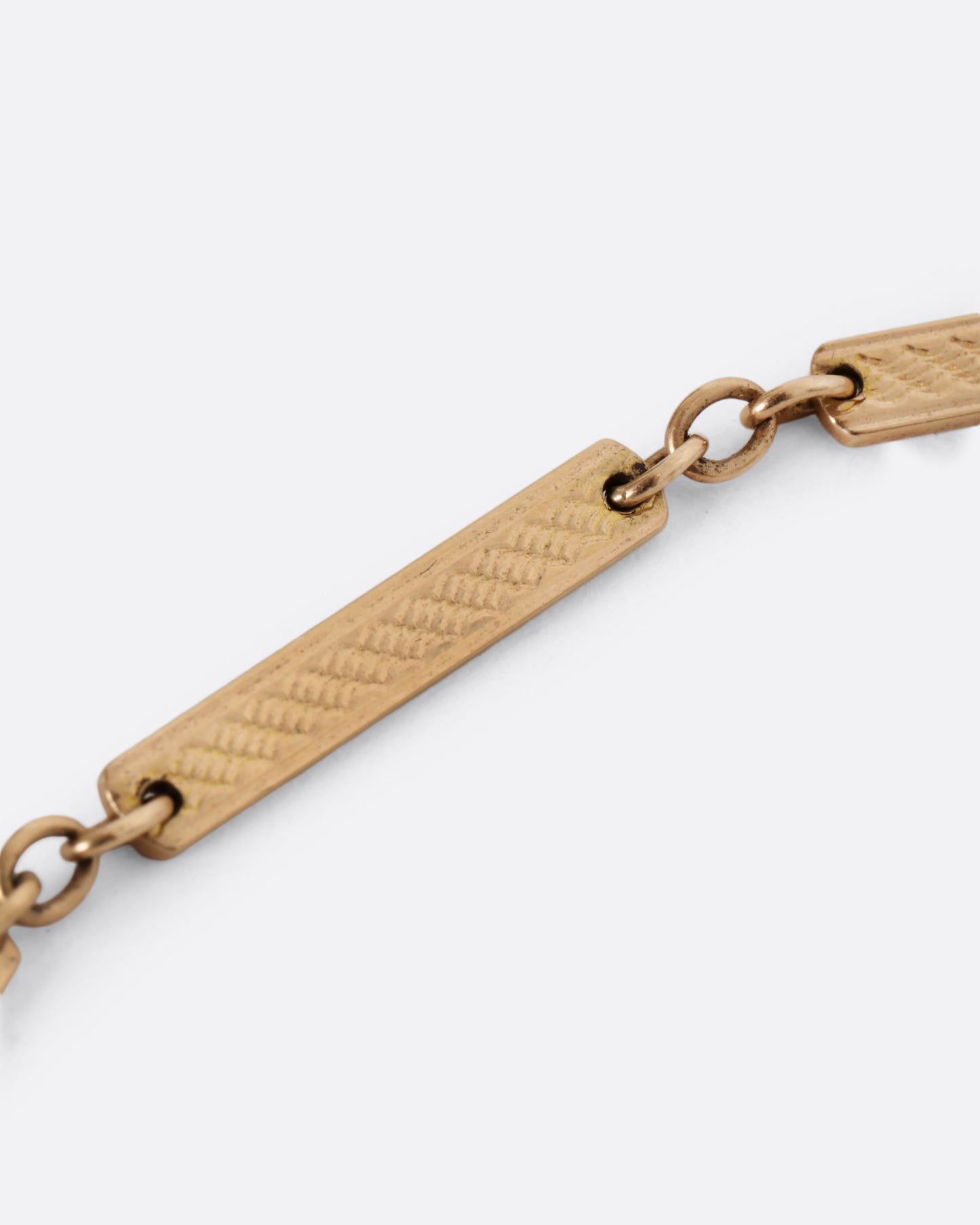 A yellow gold watch chain with textured elongated bar links. View of the chain up close.