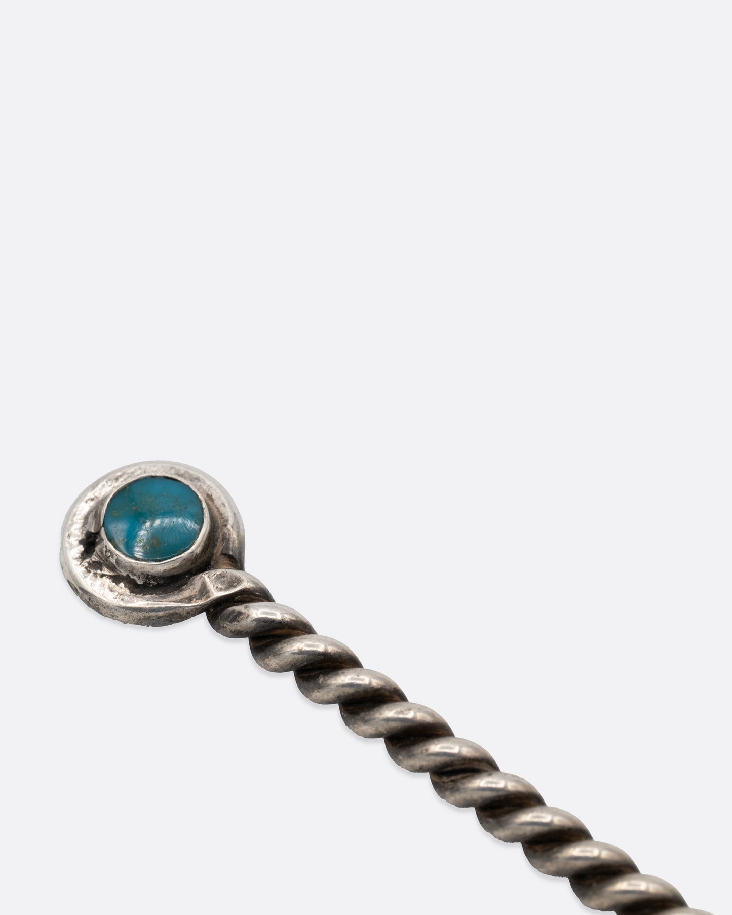 A close up of a two pronged silver olive pick with a twisted handle and round turquoise stone at the bottom. 