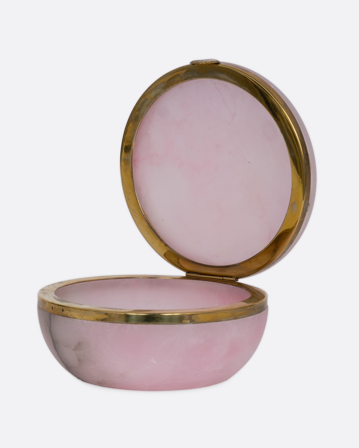 A round pink alabaster box with gold edges and a seashell shaped clasp, shown from the side open.