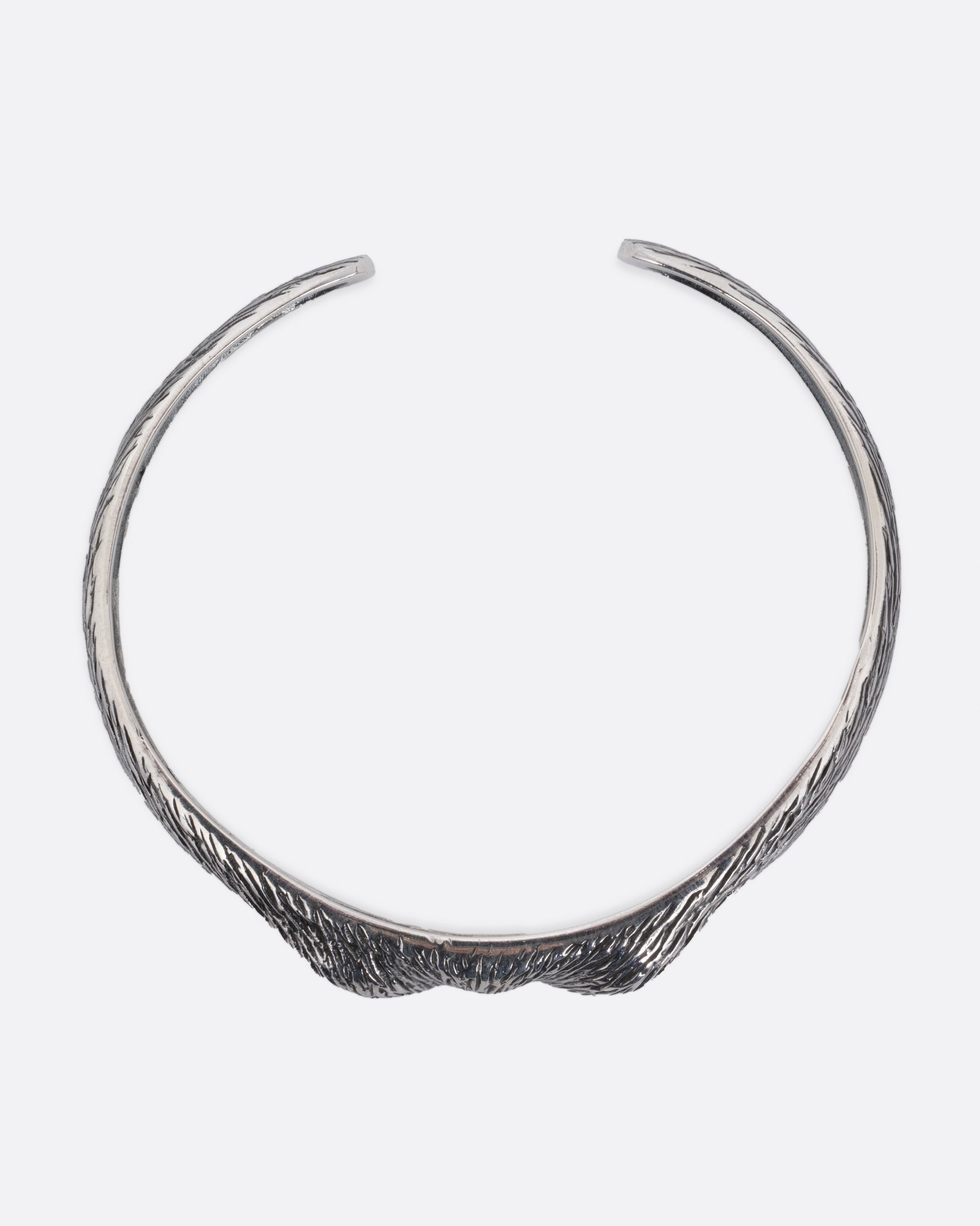 A silver bracelet with blue glass eyes and an all-over carved texture. Shown from the top.