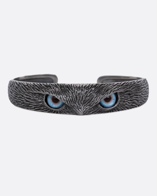 A silver bracelet with blue glass eyes and an all-over carved texture. Shown from the front.