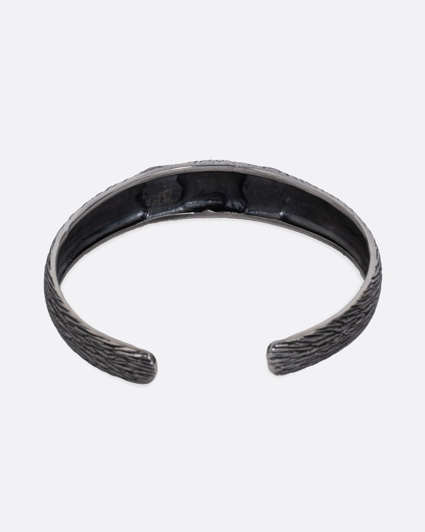 A silver bracelet with blue glass eyes and an all-over carved texture. Shown from the back.