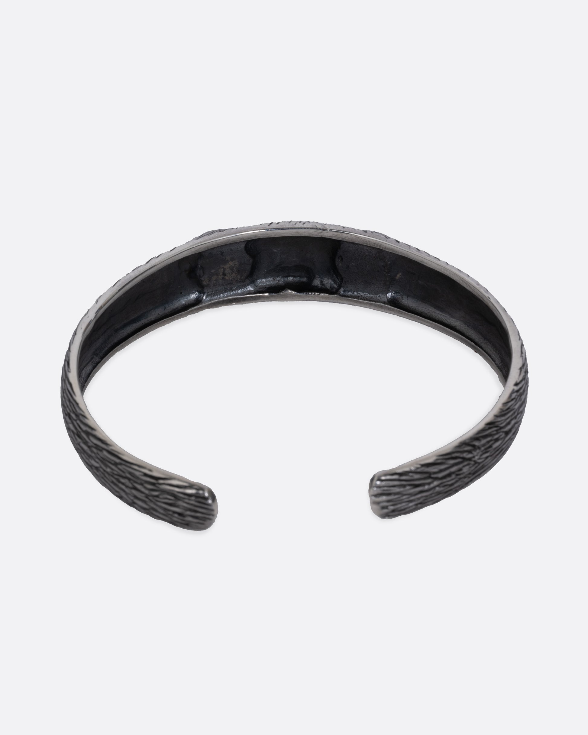 A silver bracelet with blue glass eyes and an all-over carved texture. Shown from the back.