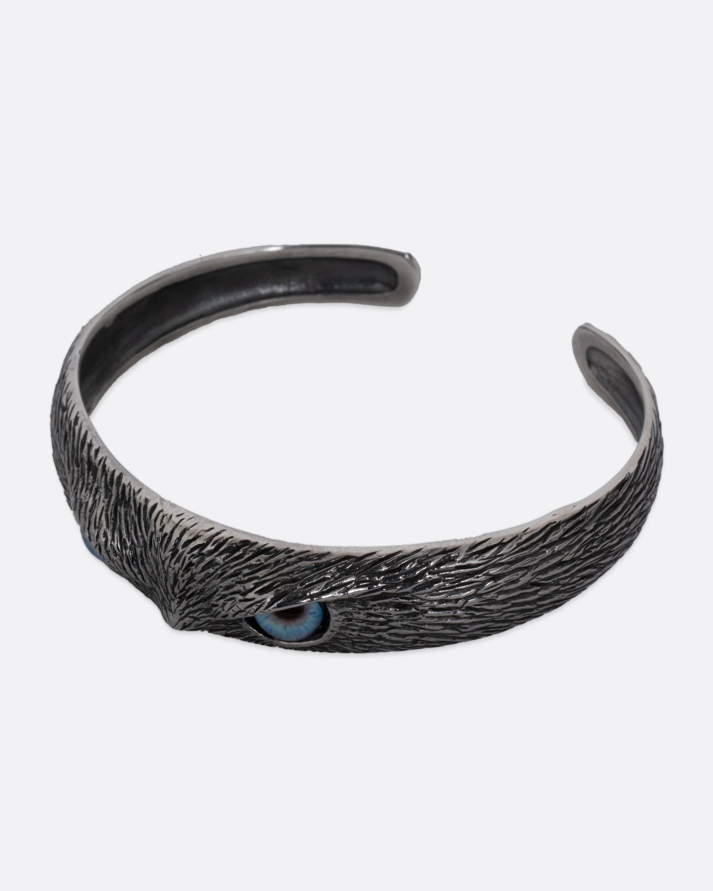 A silver bracelet with blue glass eyes and an all-over carved texture. Shown from the side.