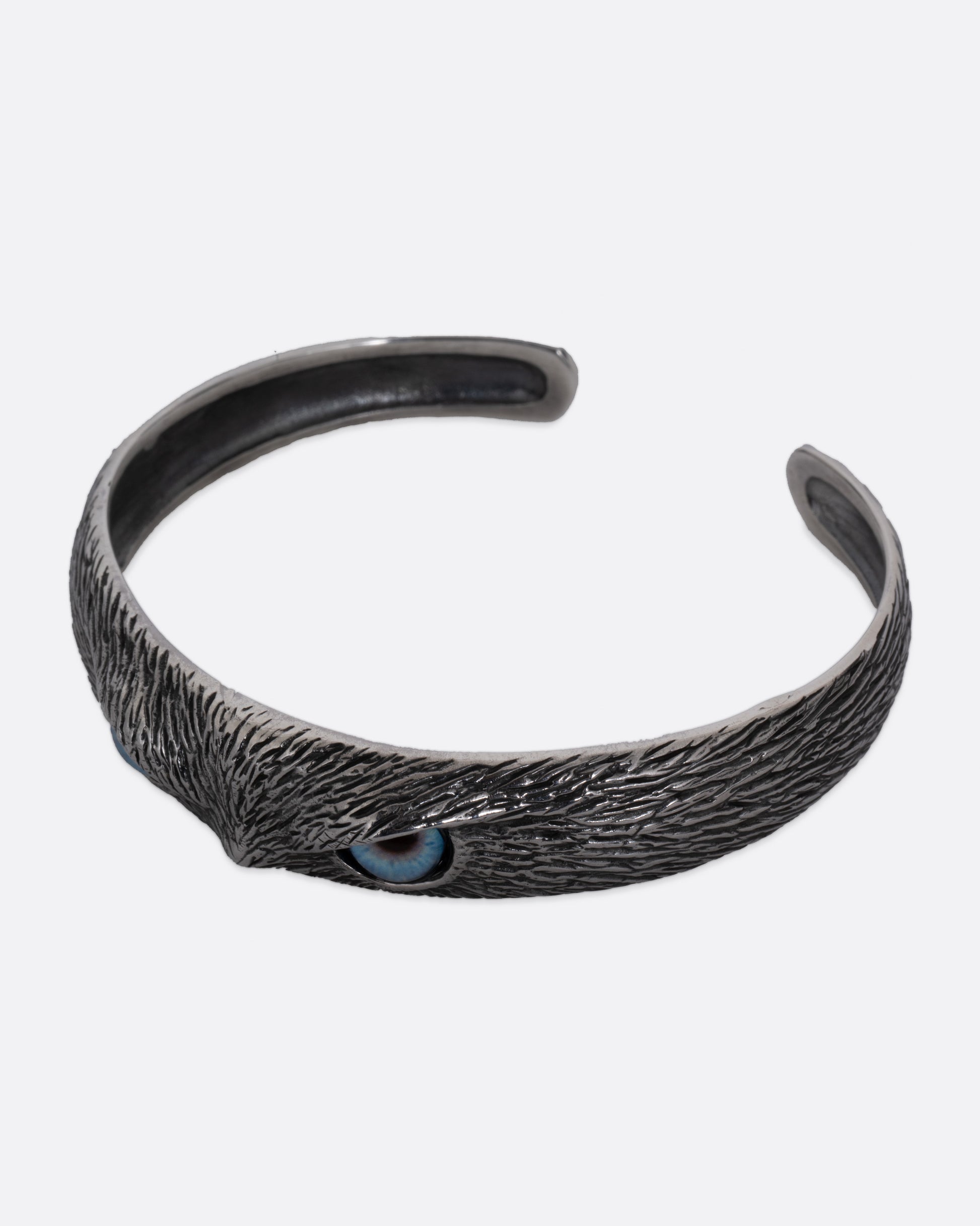 A silver bracelet with blue glass eyes and an all-over carved texture. Shown from the side.