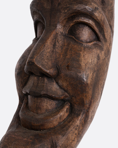 A close up of a wooden crescent moon takaan sculpture with a face.